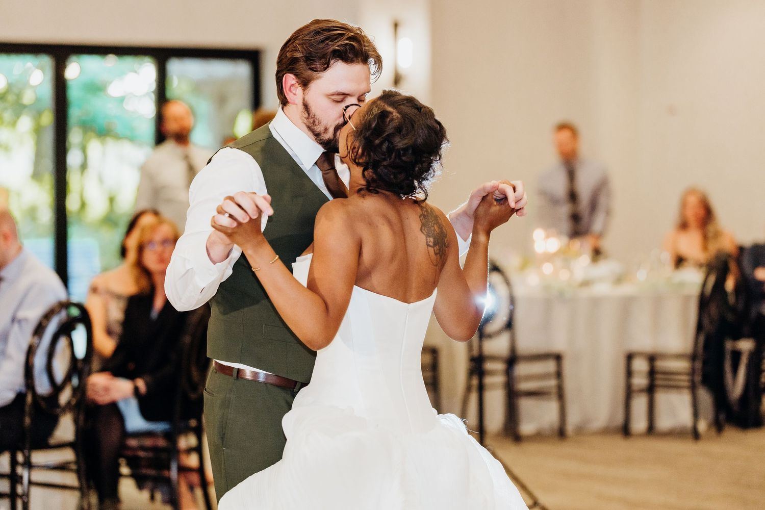 Wedding reception dance in elegant ballroom with hardwood floors and chandelier lighting.