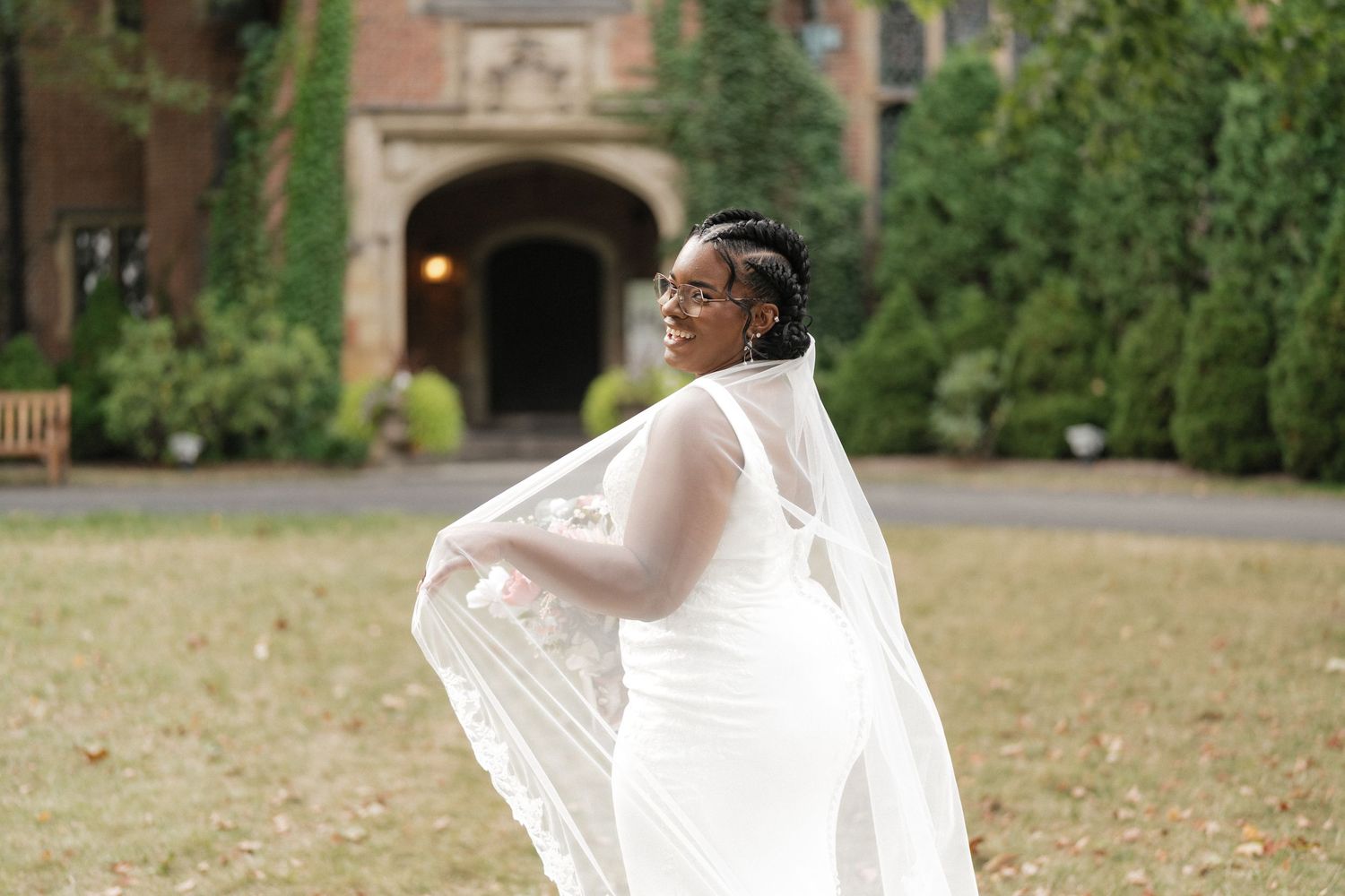 Bride in flowing white dress walking through garden pathway with trailing veil.