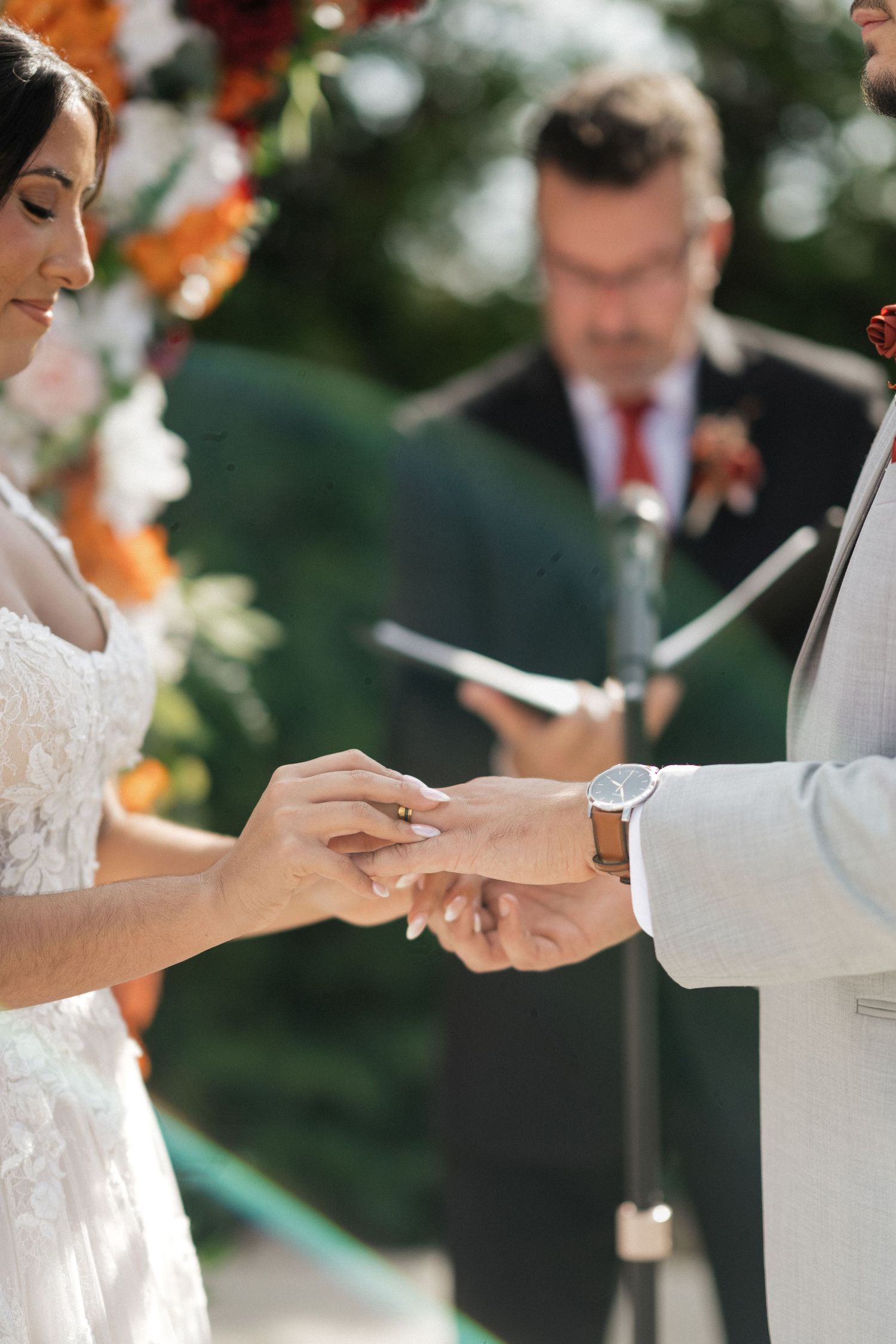 Wedding ceremony ring exchange moment under floral arch with orange and white flowers.