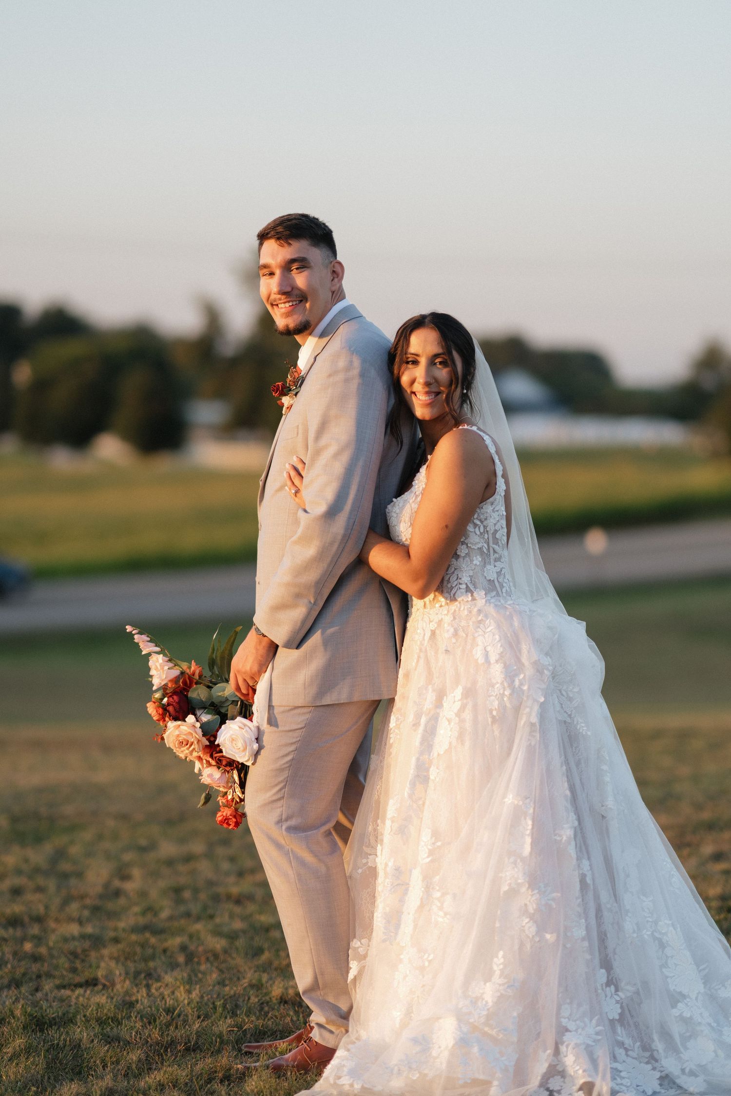 Sunset wedding portraits of a couple in light colored attire walking through an open field.
