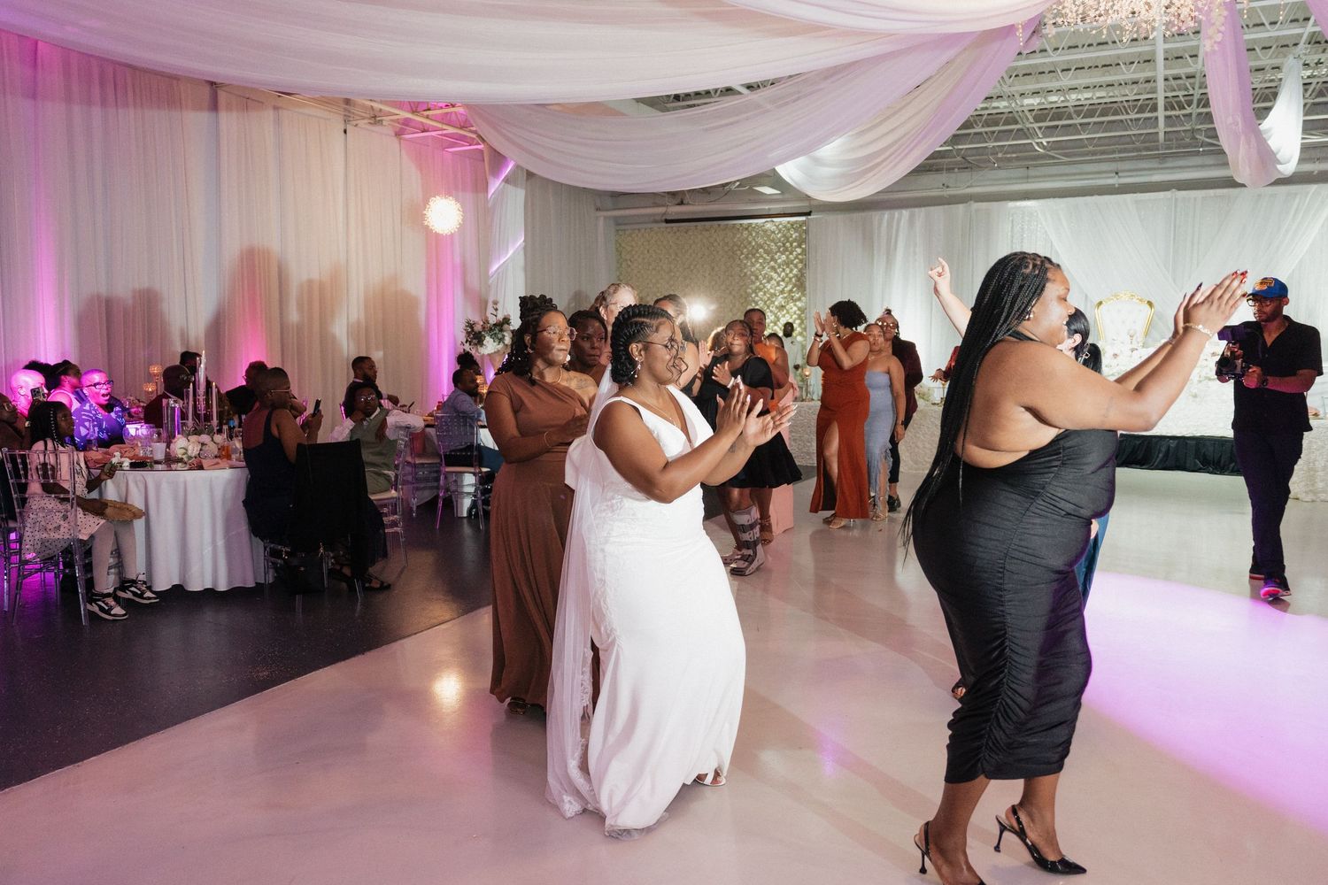 Wedding reception dance floor with pink lighting and white draping decorations.