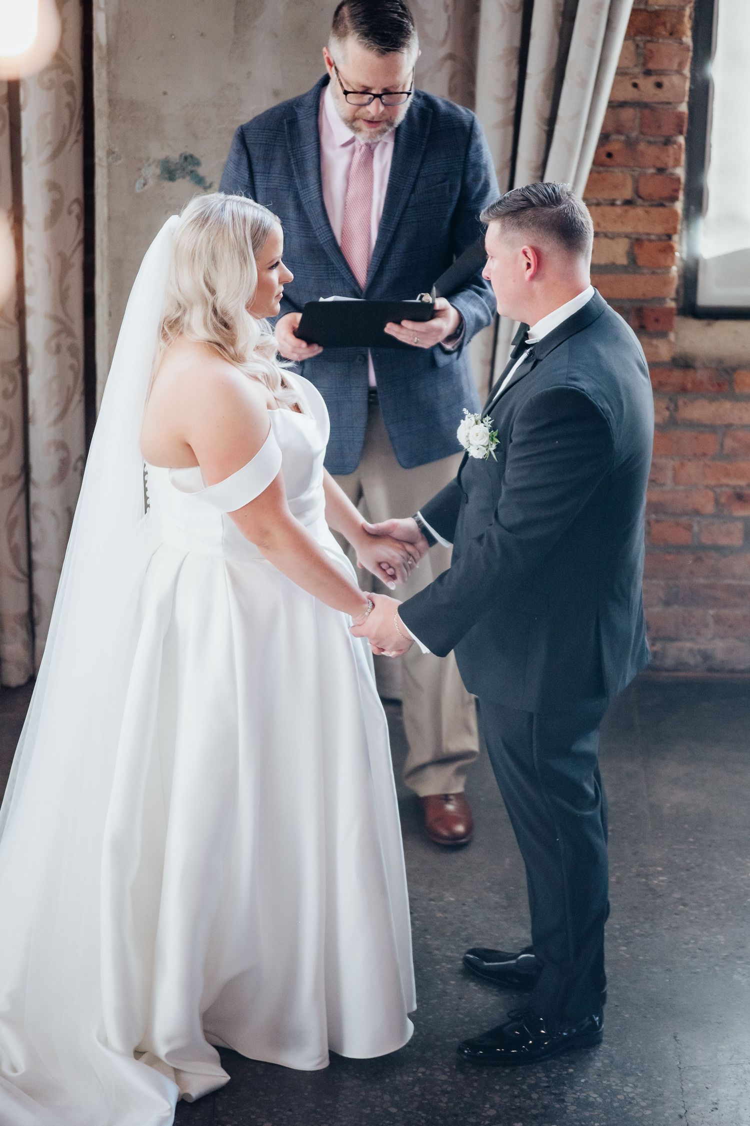 Wedding ceremony taking place in an industrial-style venue with exposed brick walls and natural light.