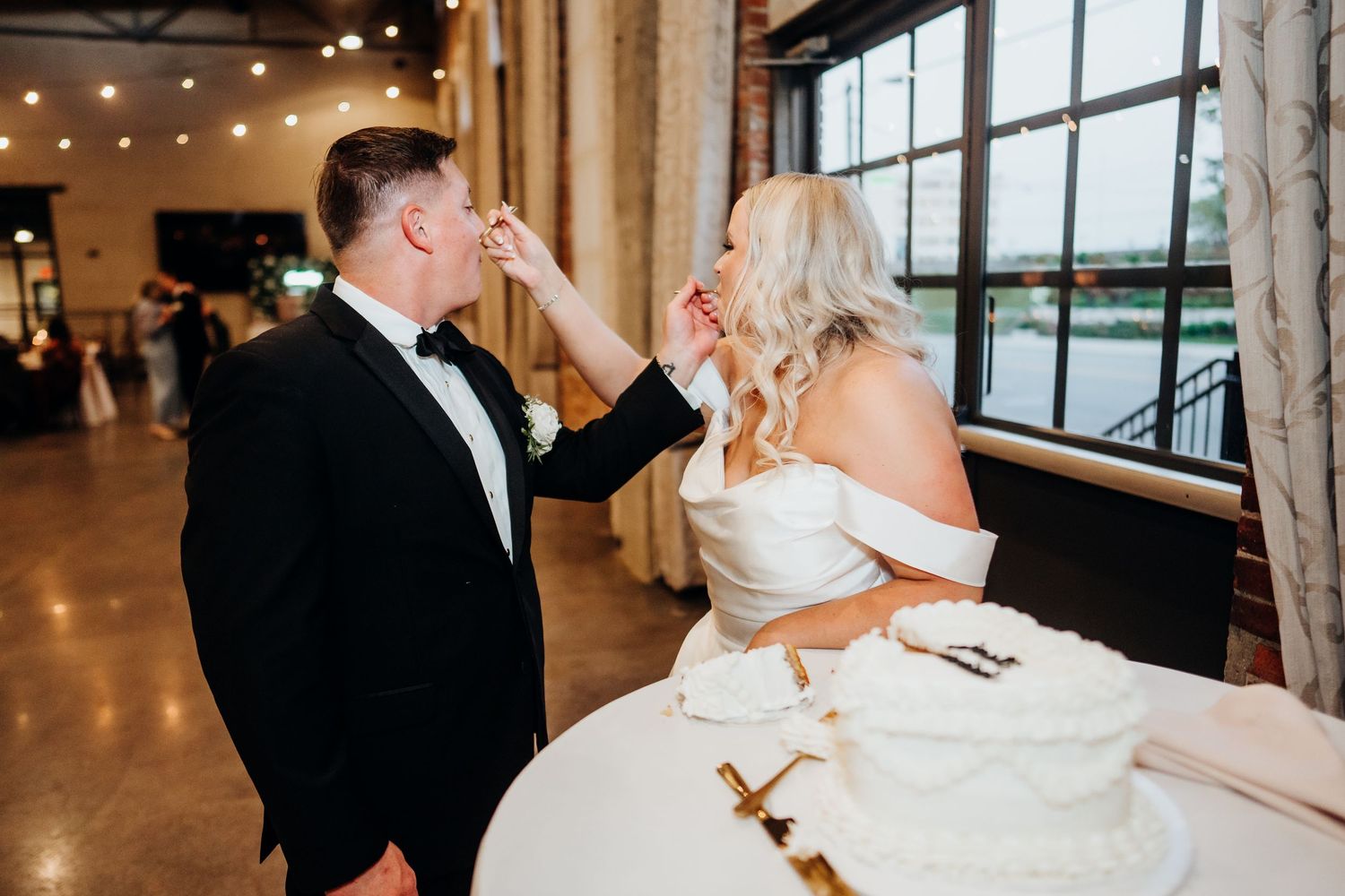 Wedding celebration in an industrial venue with string lights and large windows.