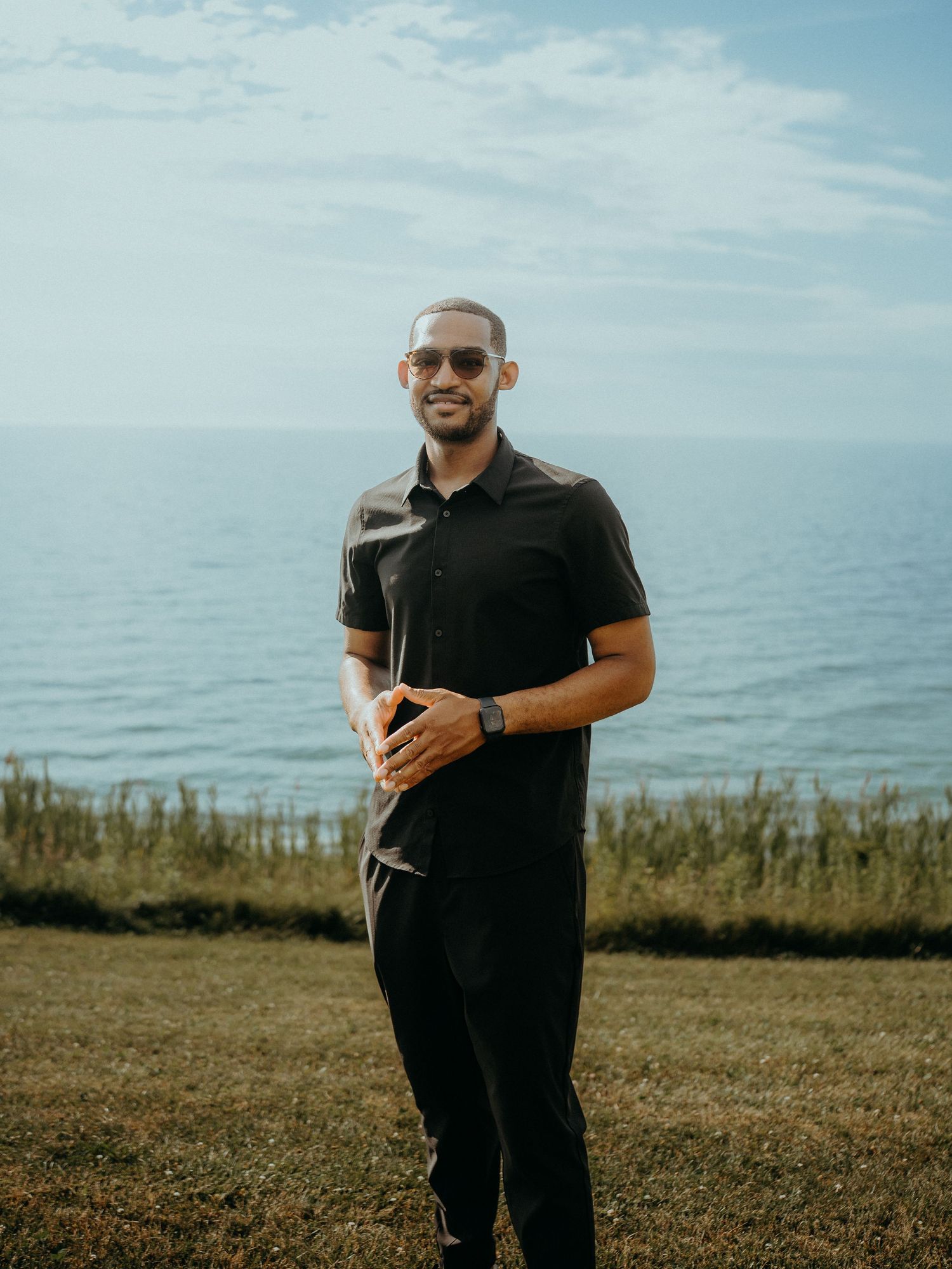 Someone wearing black clothing stands in a grassy field against a serene blue sky backdrop.