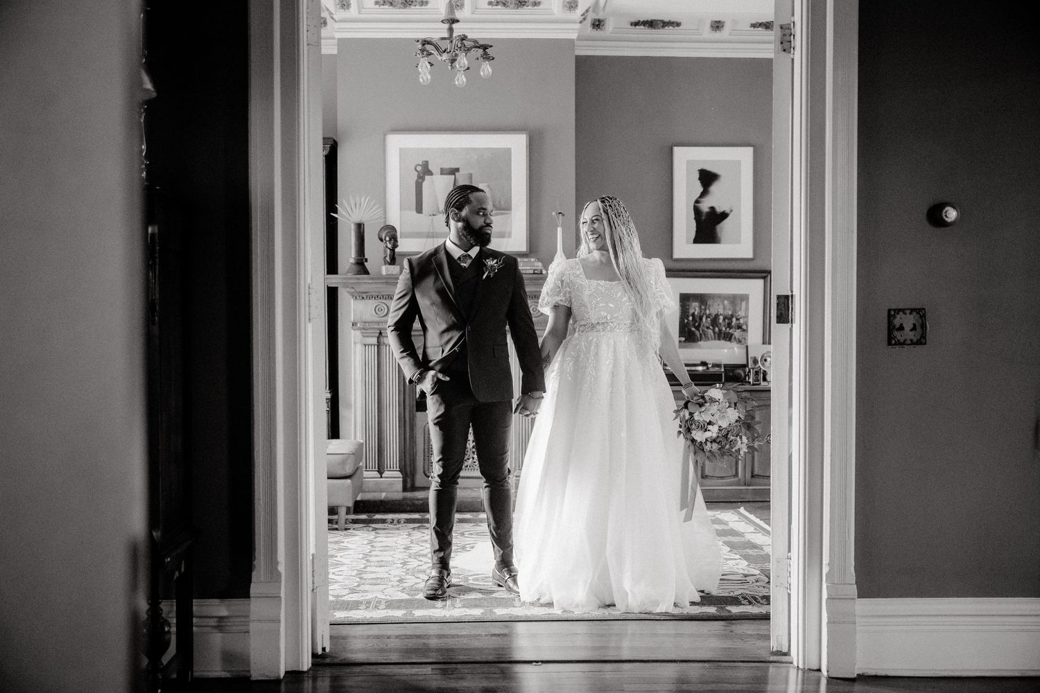 A black and white wedding photograph showing a couple walking through an elegant doorway in formal attire.