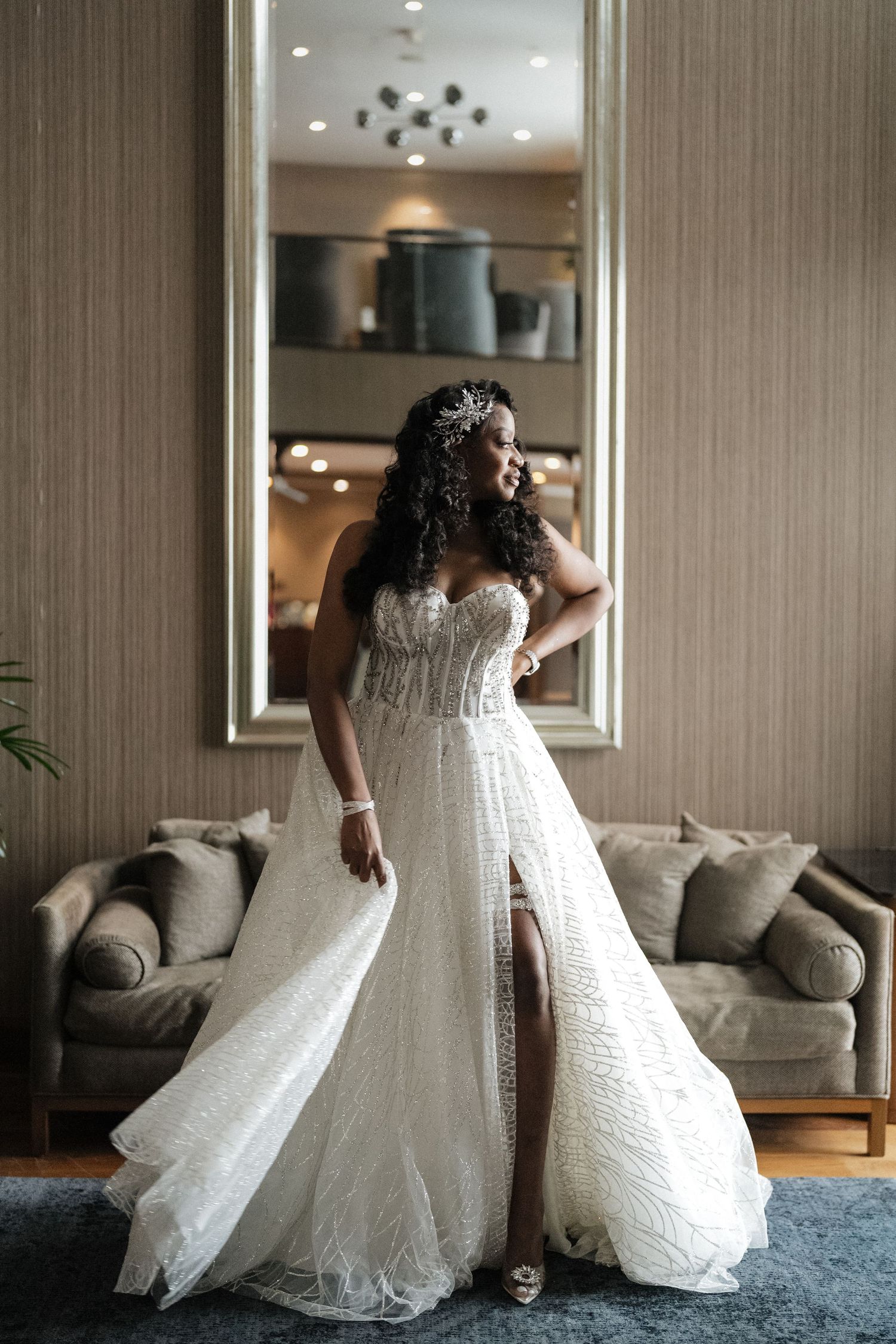 A bride in a stunning white beaded wedding gown twirls gracefully on a blue carpet in front of a modern sofa.