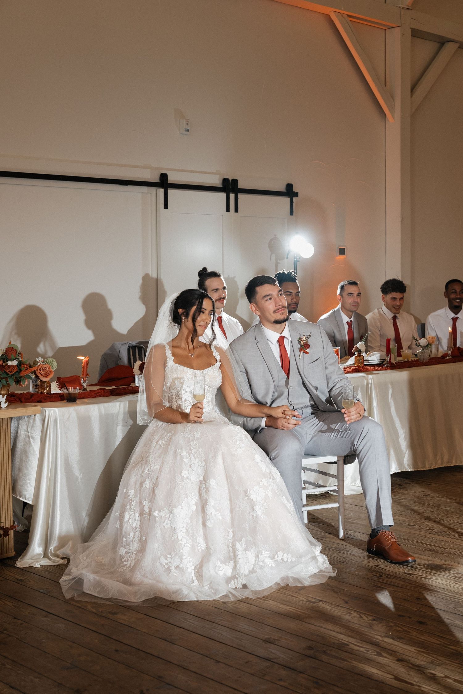 Wedding party poses for photos in a rustic venue with wooden floors and white walls.