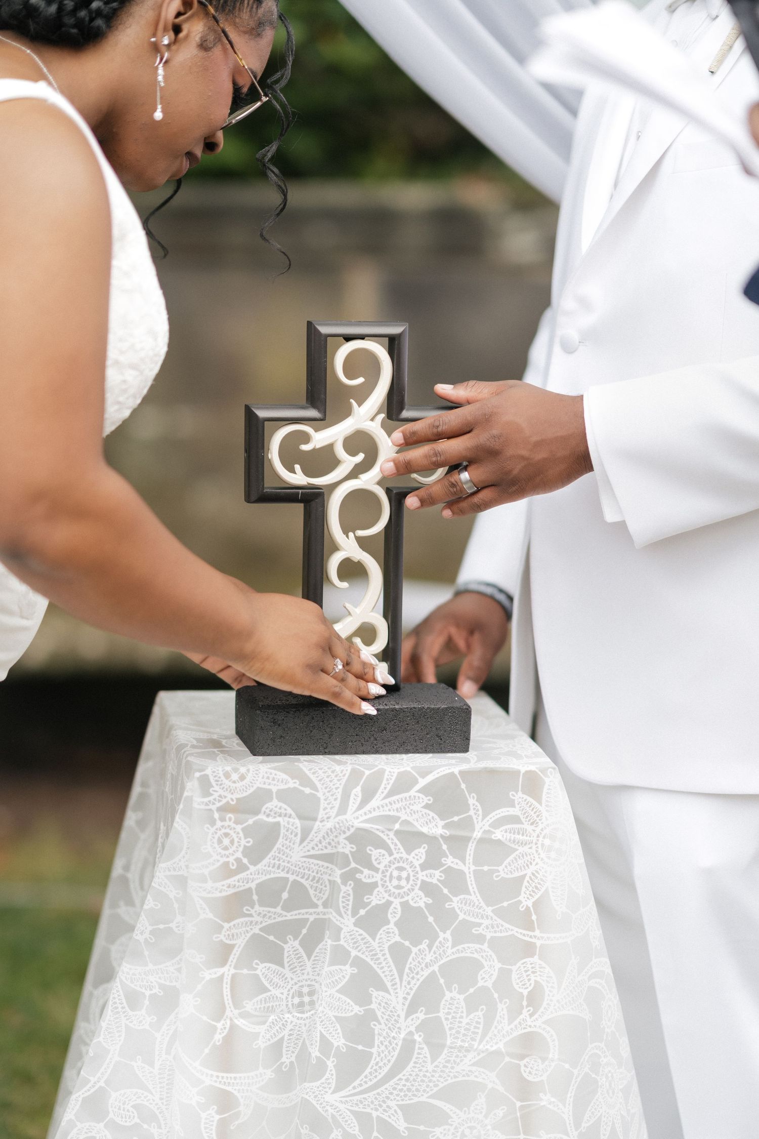 Wedding couple holding decorative cross during outdoor ceremony ritual.
