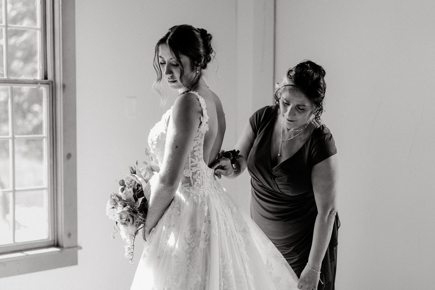 Bride in white lace dress prepares for her wedding day with assistance.
