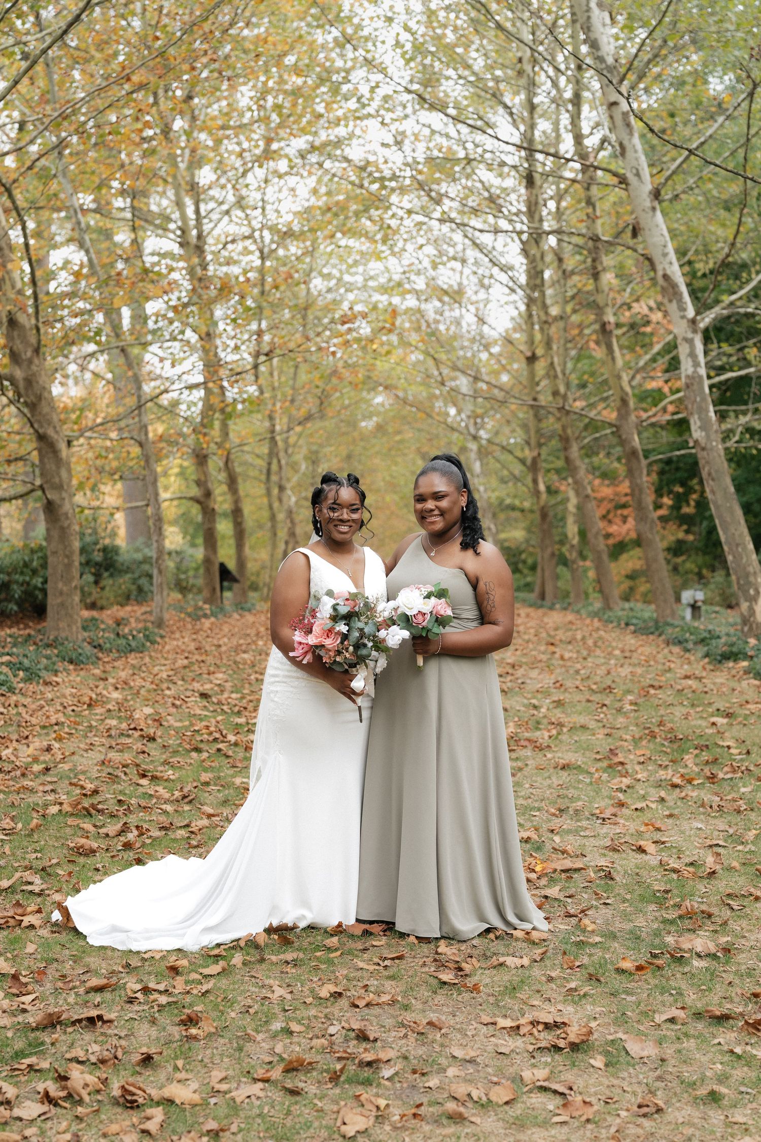 Wedding party poses among fallen autumn leaves in a wooded setting.