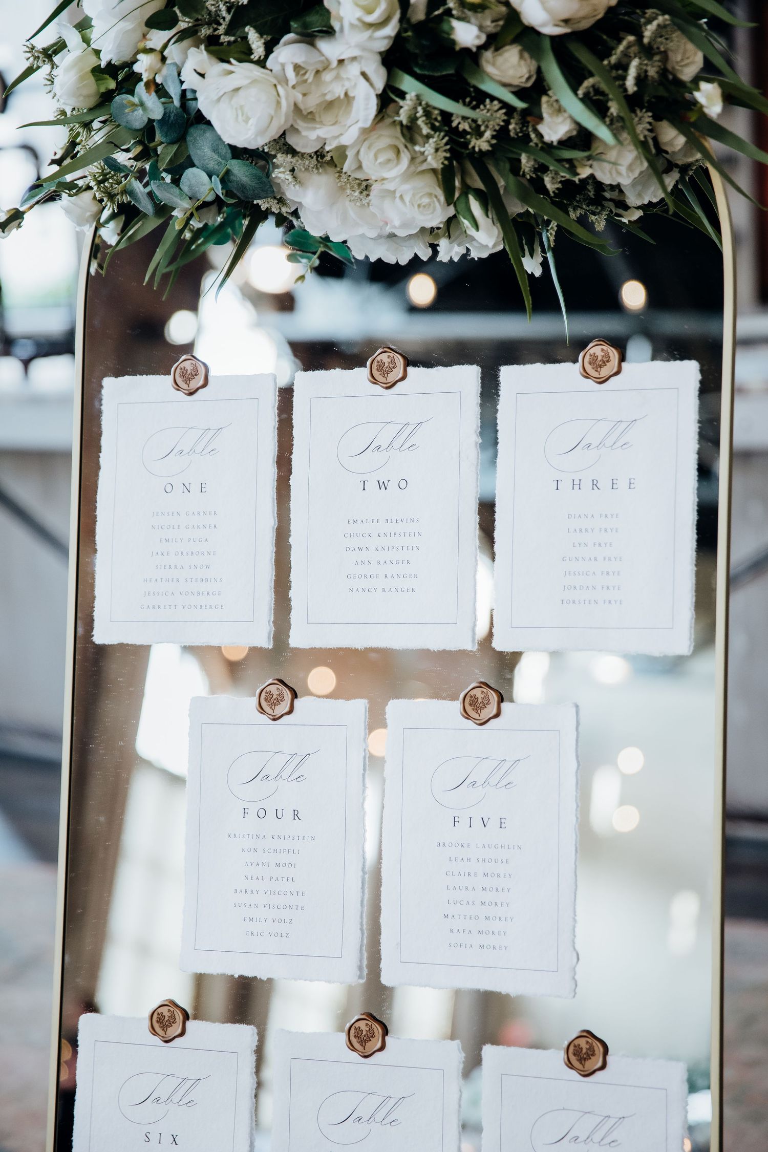 Elegant wedding seating chart with white cards and floral decorations displaying table assignments.