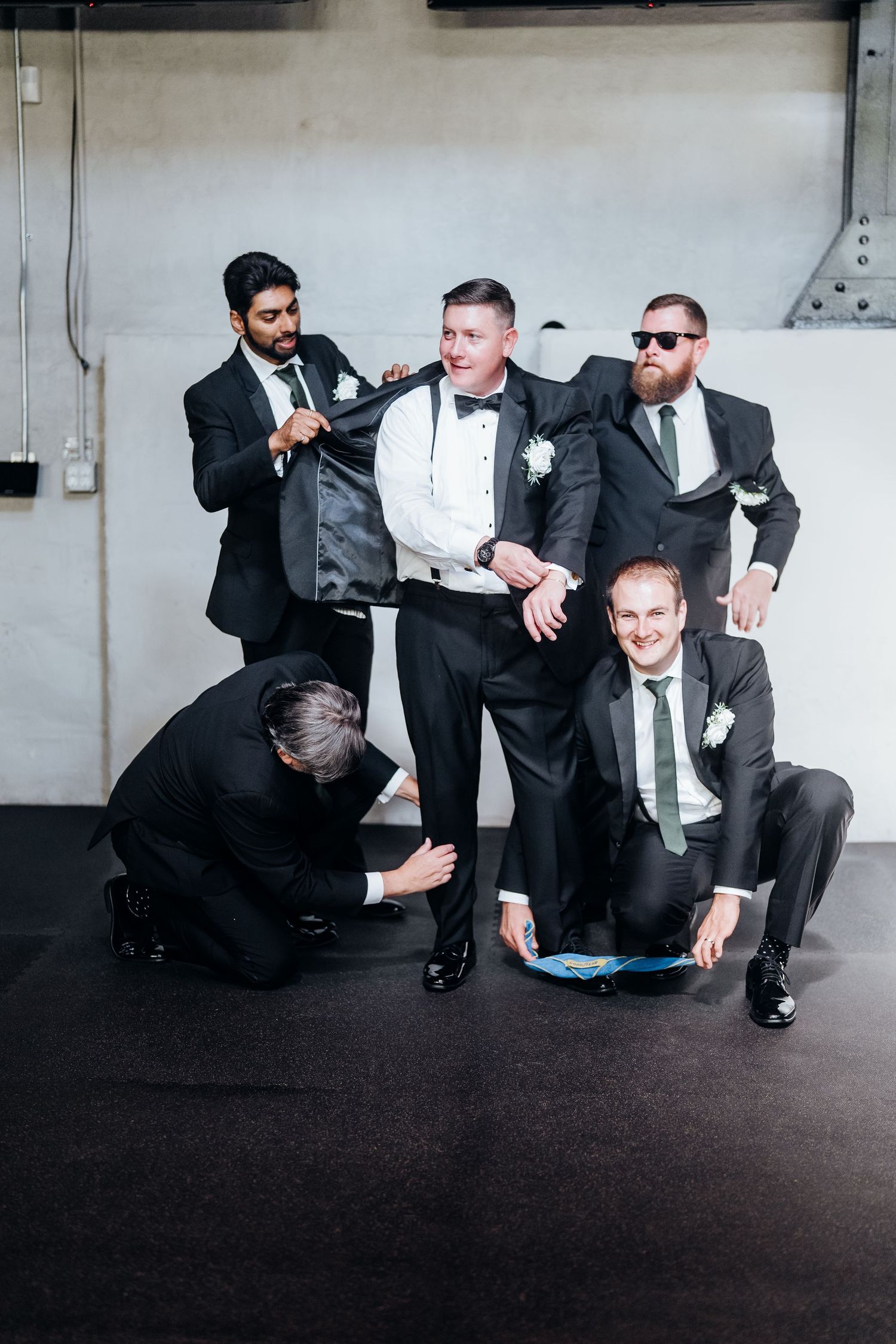 Groomsmen in black suits playfully posing on the ground in a creative photo sequence.