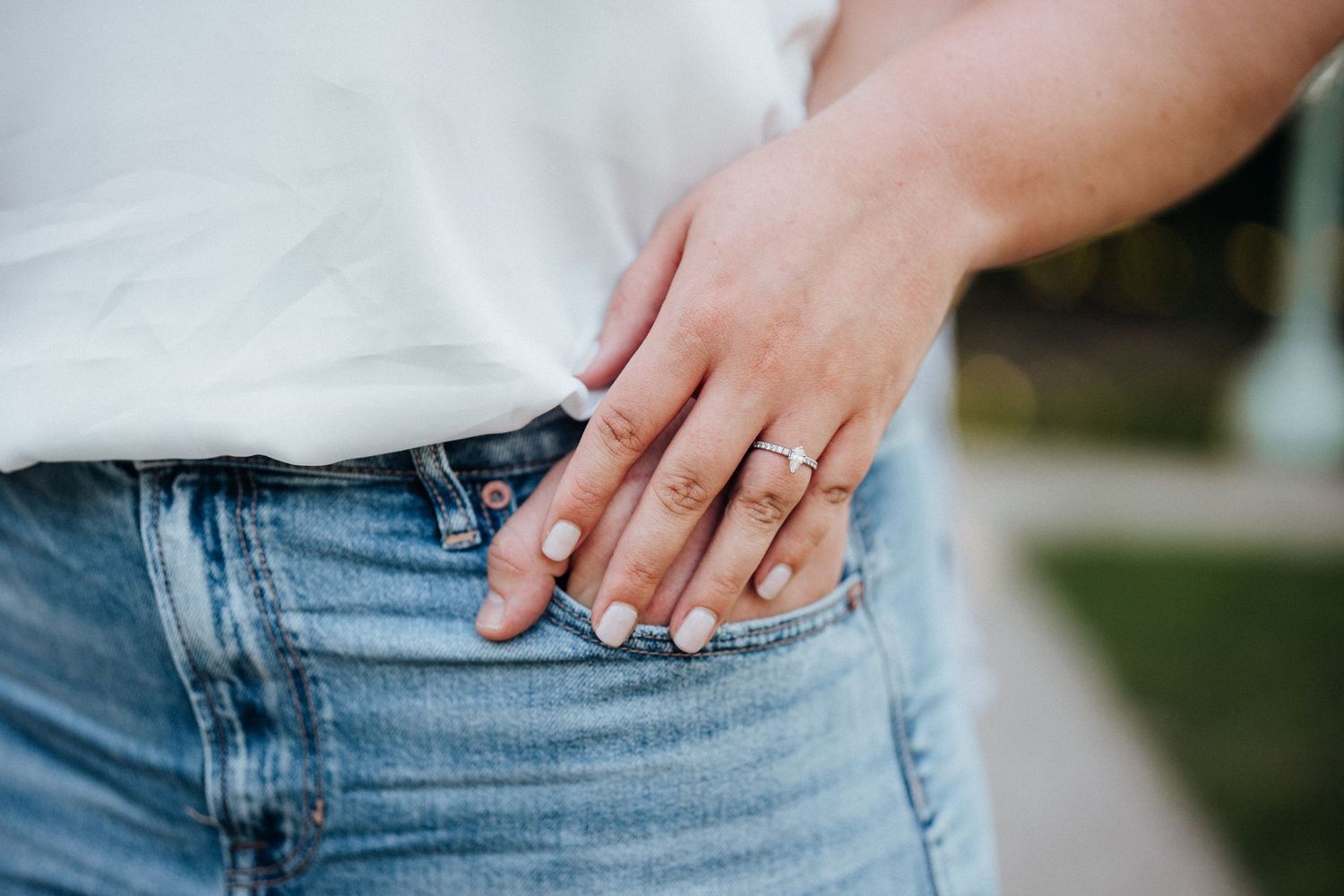 A close-up shot of a hand displaying an engagement ring against denim jeans.