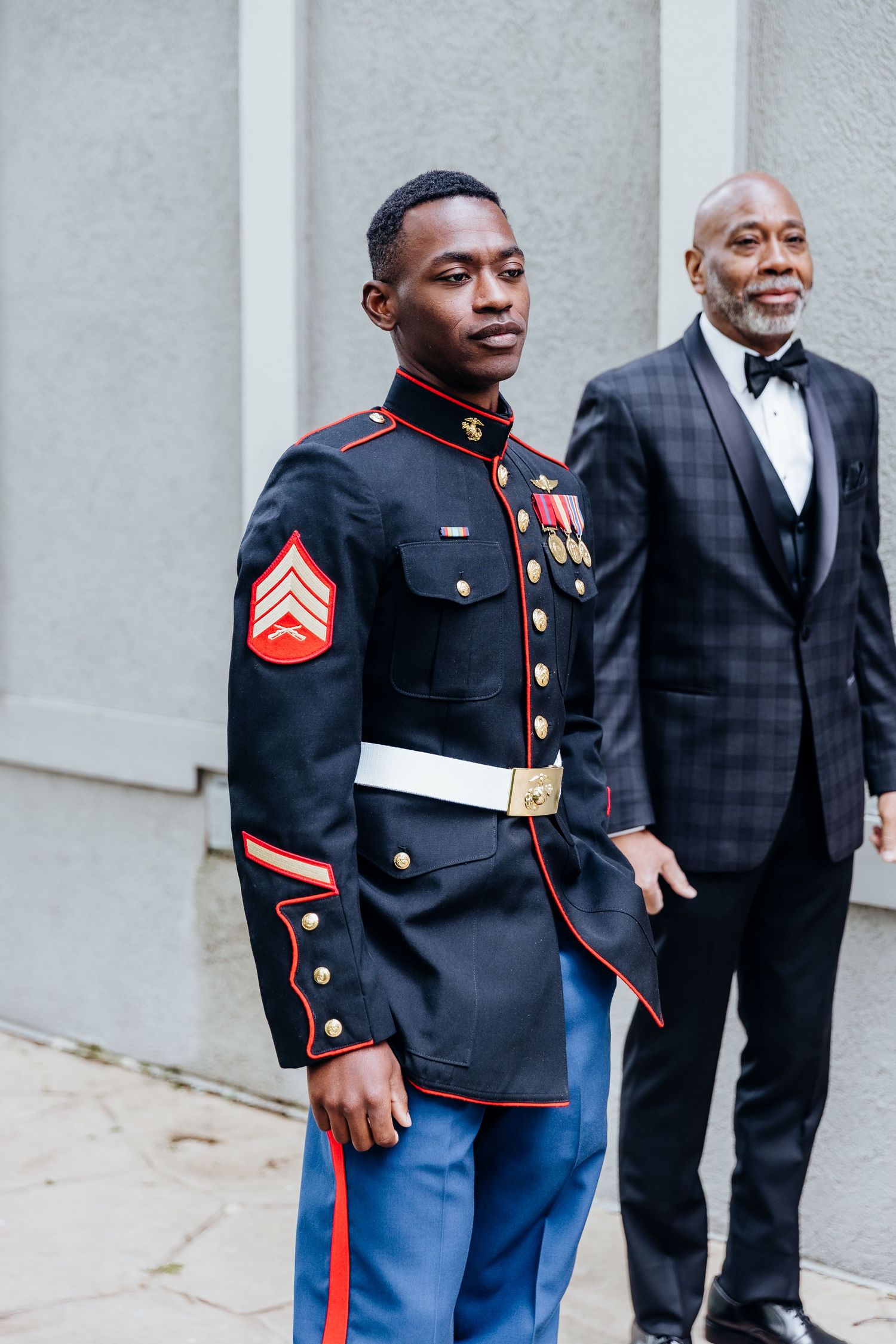 Marine in dress uniform stands proudly next to person in formal suit at wedding event.