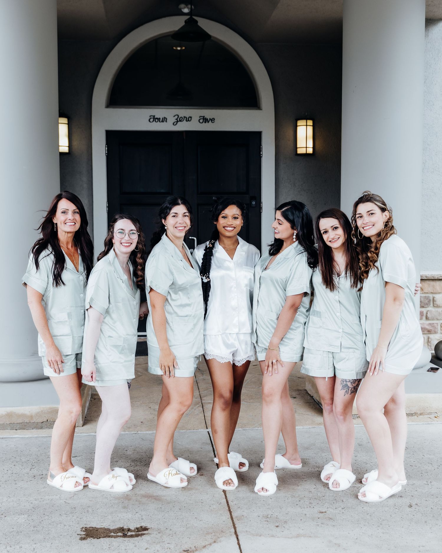 Group wearing matching white rompers and sneakers pose in front of an arched doorway.