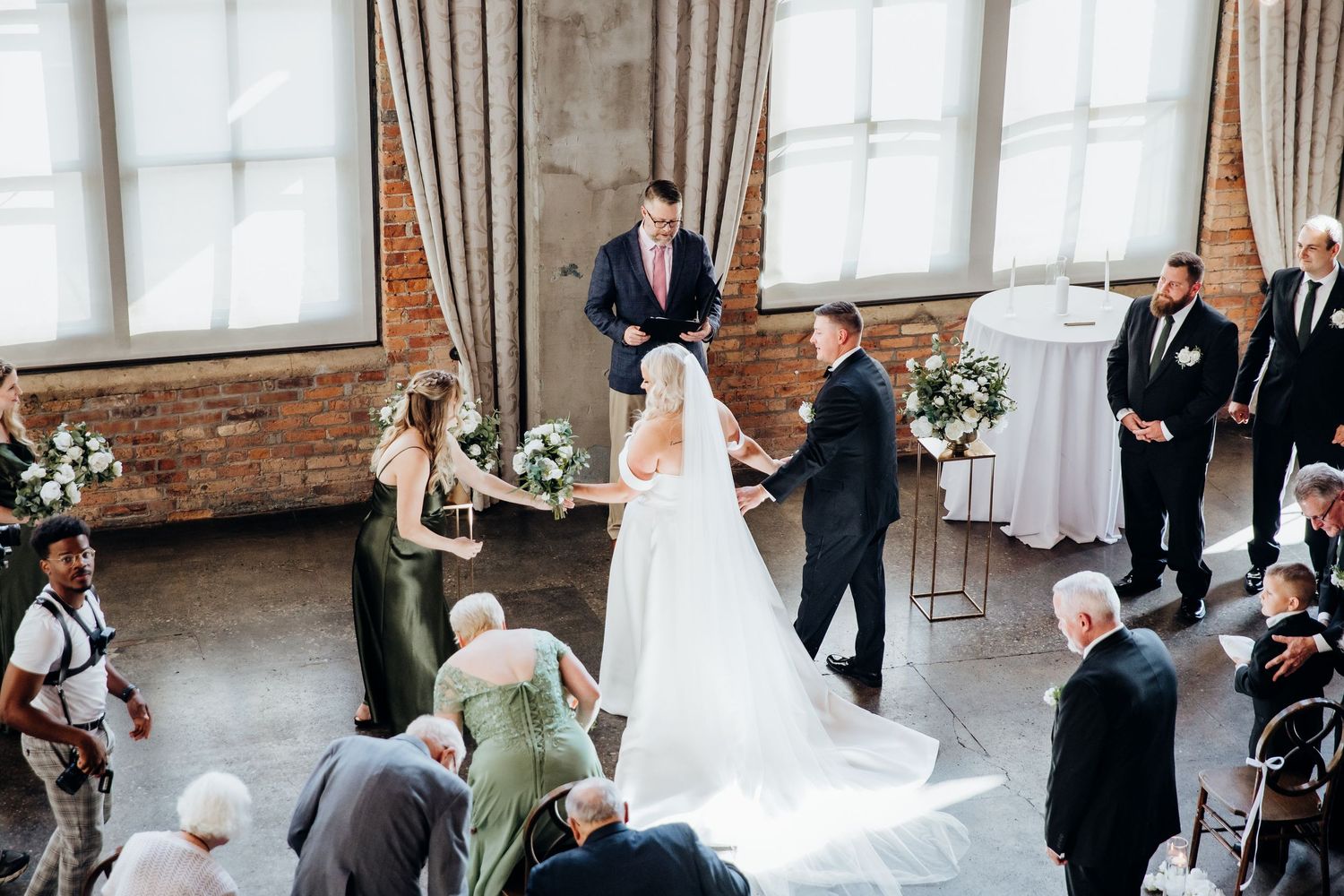 Wedding ceremony in progress inside a rustic brick venue with large windows.