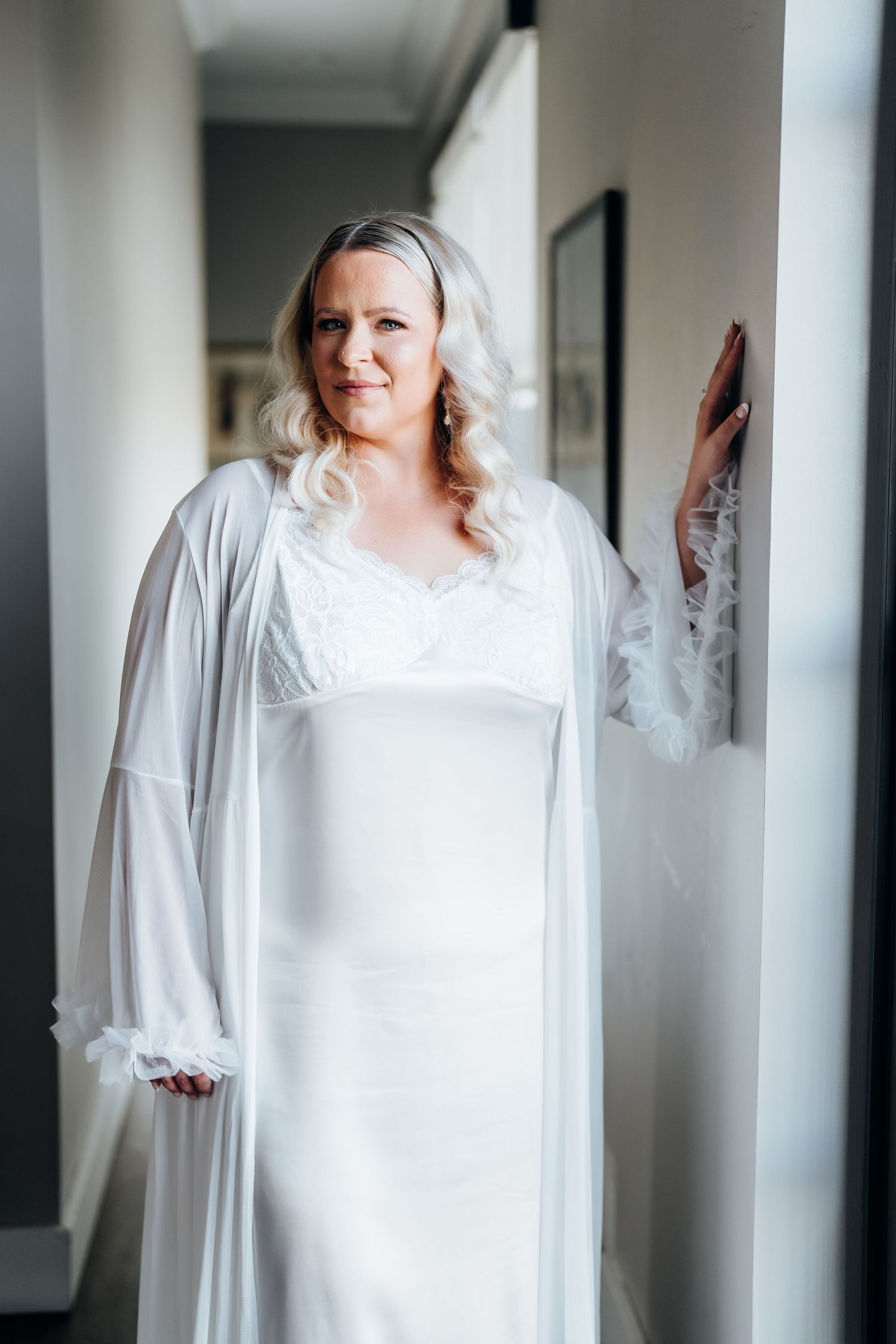 Person in a flowing white robe standing in a bright hallway.