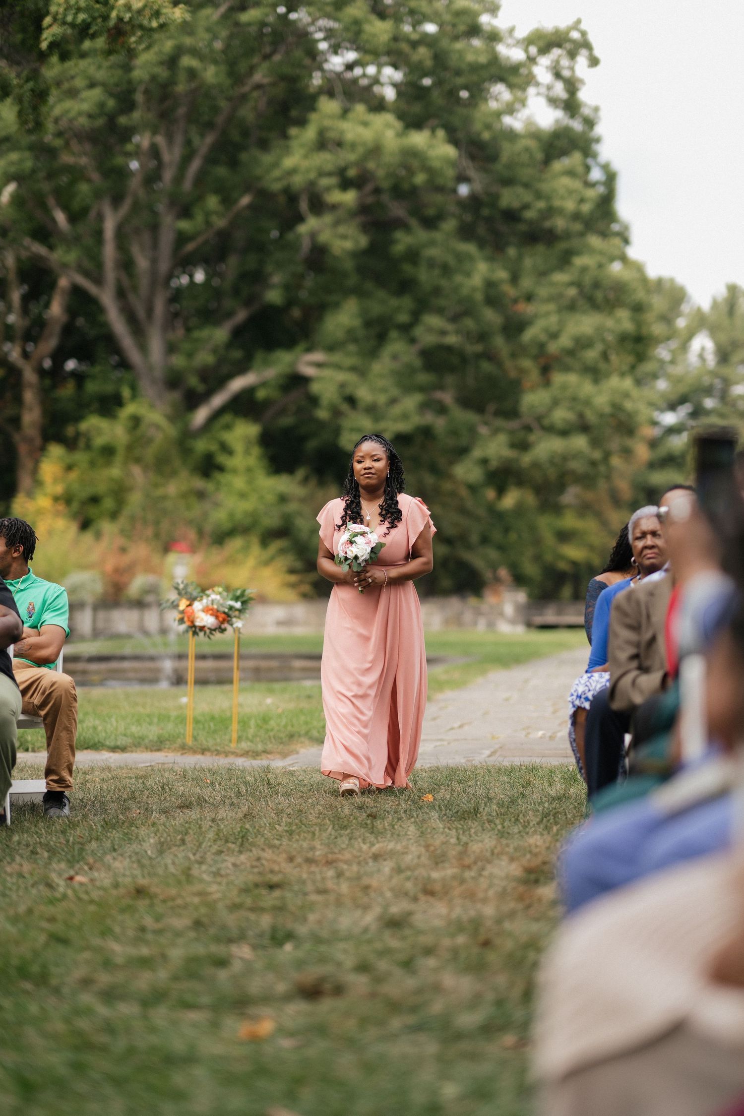 Wedding party members in pink dresses walking across a sunny outdoor field during ceremony.