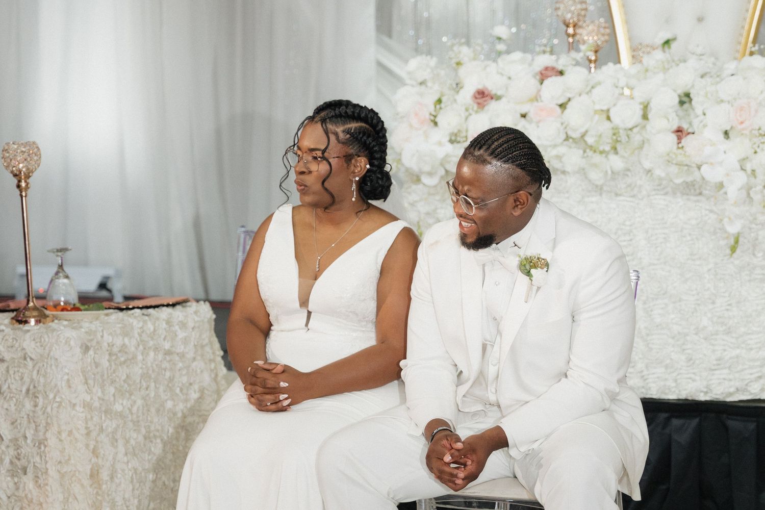 Couple shares intimate moment at wedding reception with white flower wall backdrop.