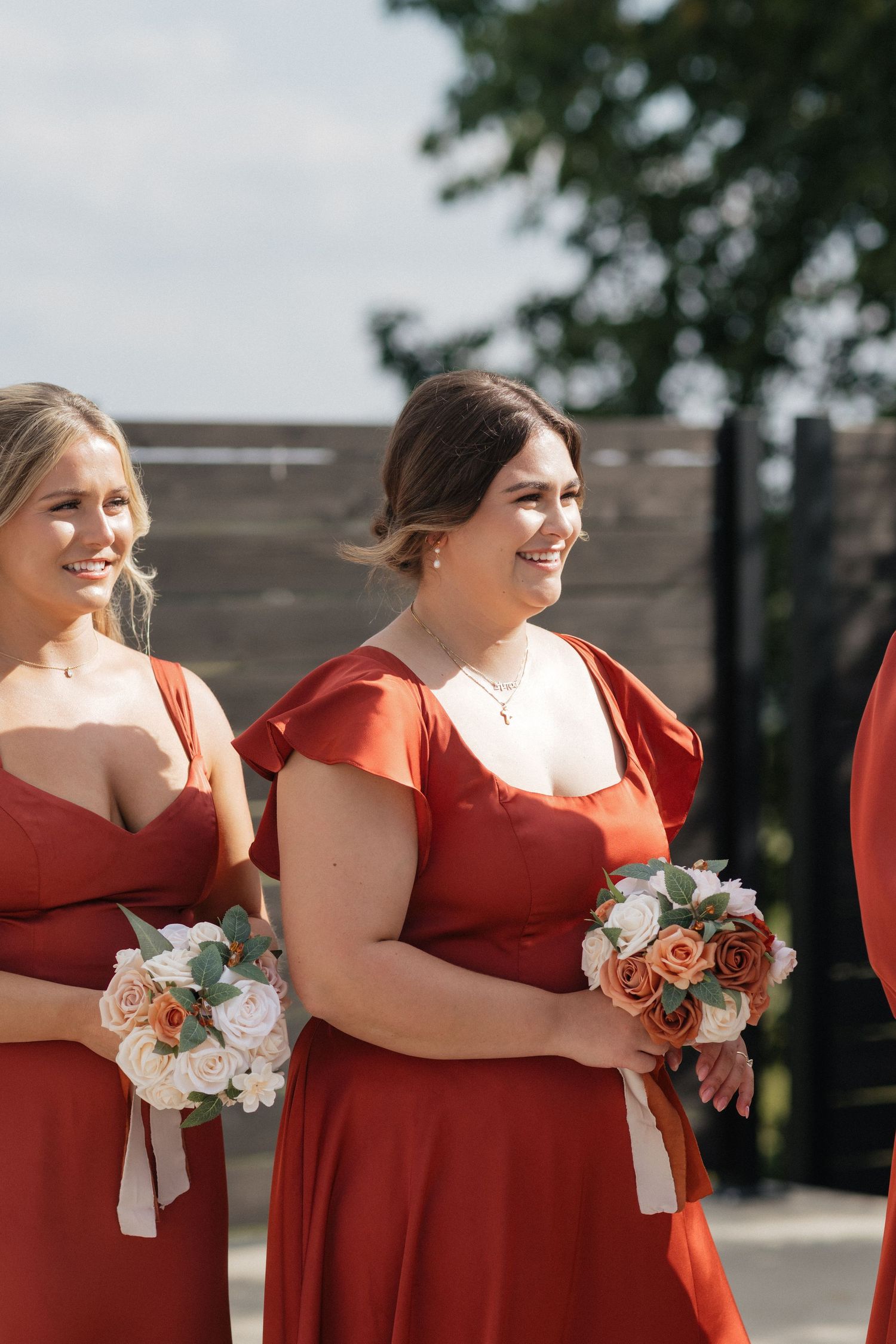 Bridesmaids in red dresses hold bouquets while standing together outdoors.
