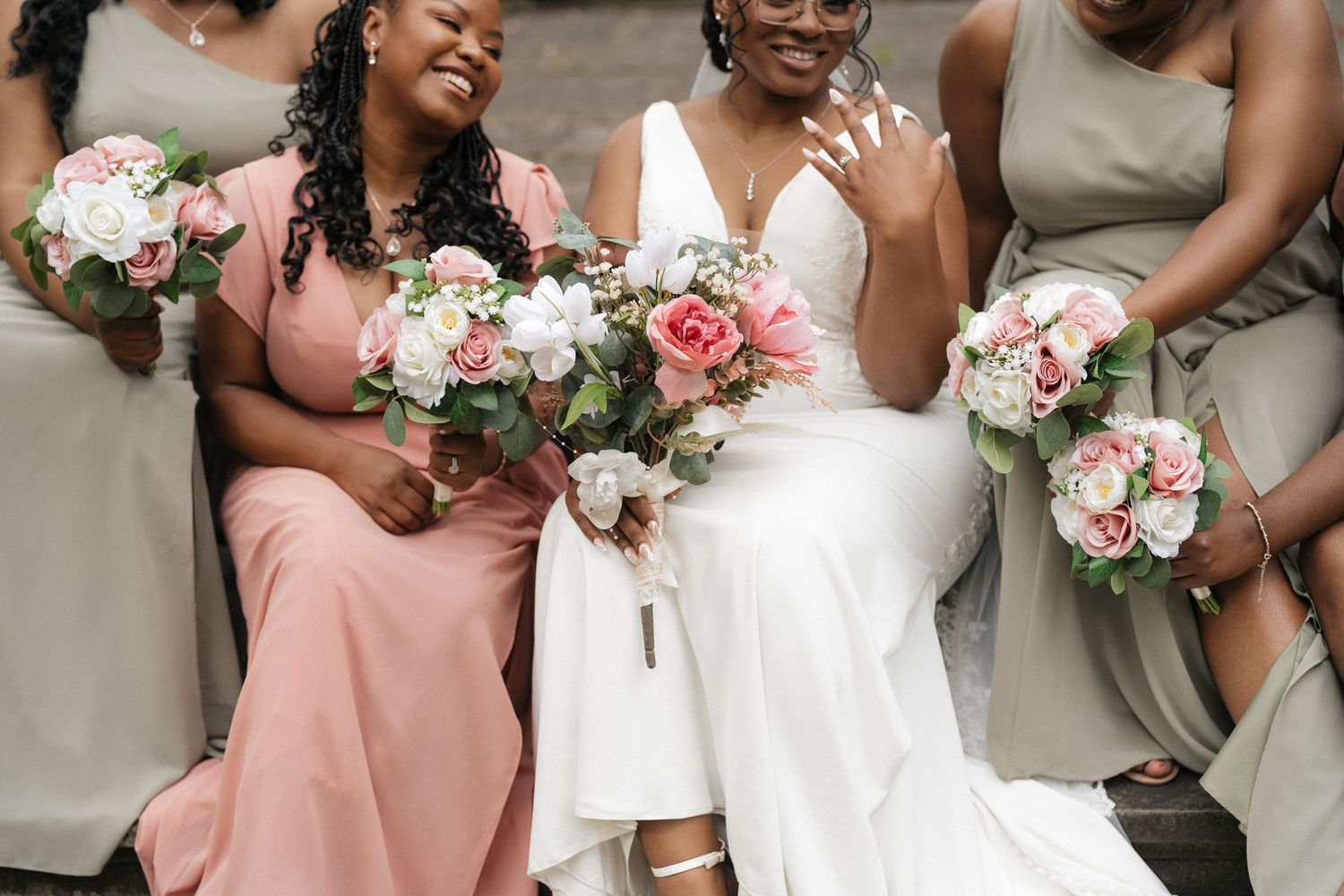 Wedding party members hold bouquets of pink and white flowers while wearing coral and white dresses.