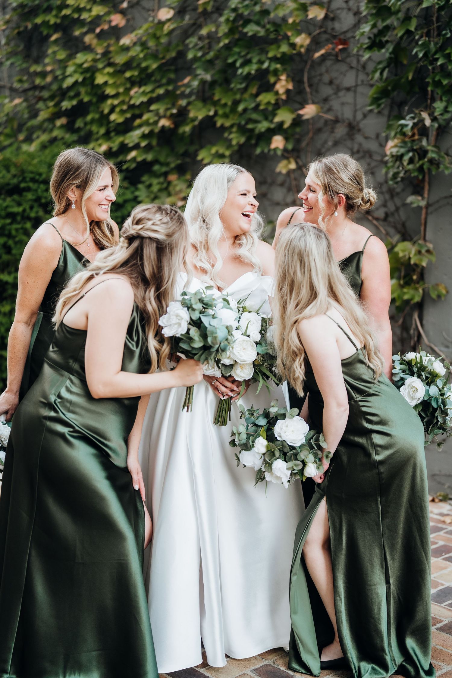 Bridesmaids in olive green dresses laughing together with the bride in white.