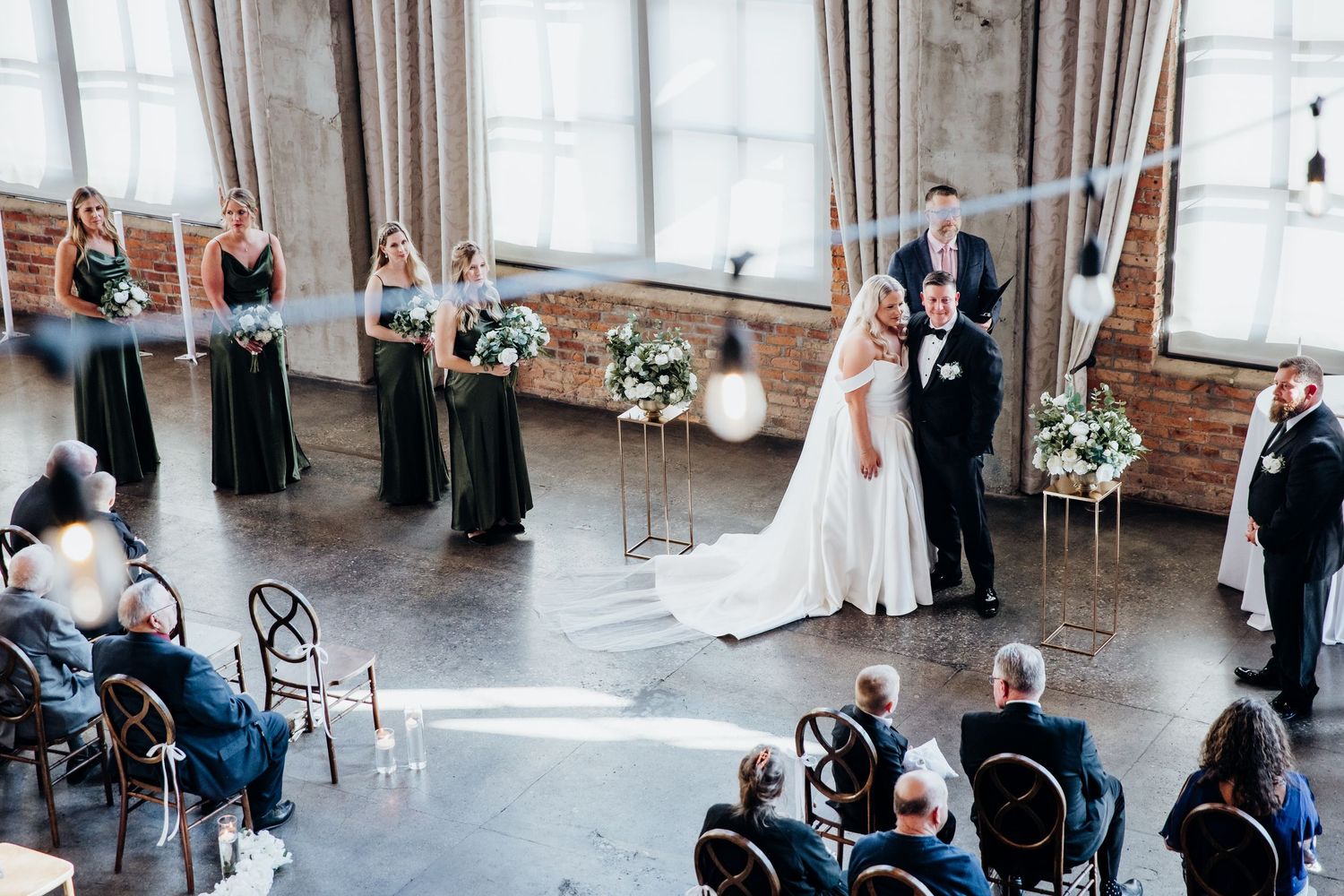 Wedding ceremony guests seated in rows at an industrial-style venue with brick walls and natural light.