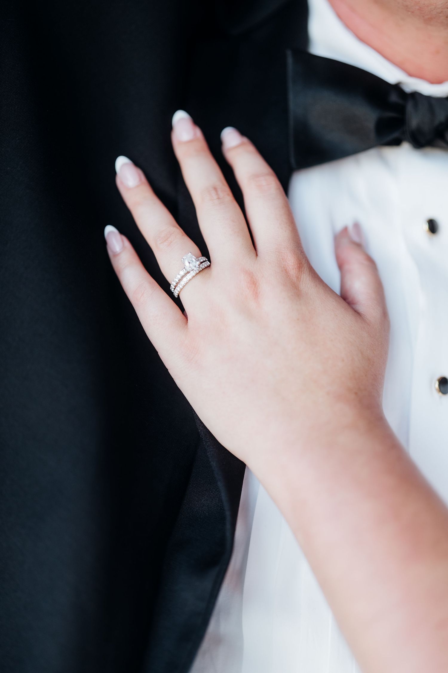 Close-up detail shots of diamond engagement ring and wedding bands on hands against a dark background.