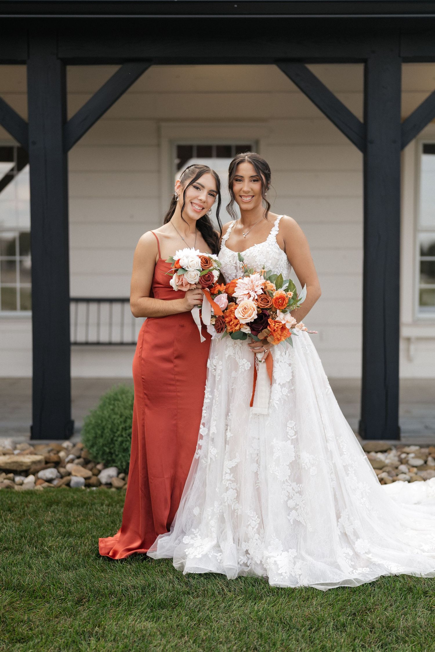 Wedding party members pose together under a covered porch with autumn-colored floral bouquets.