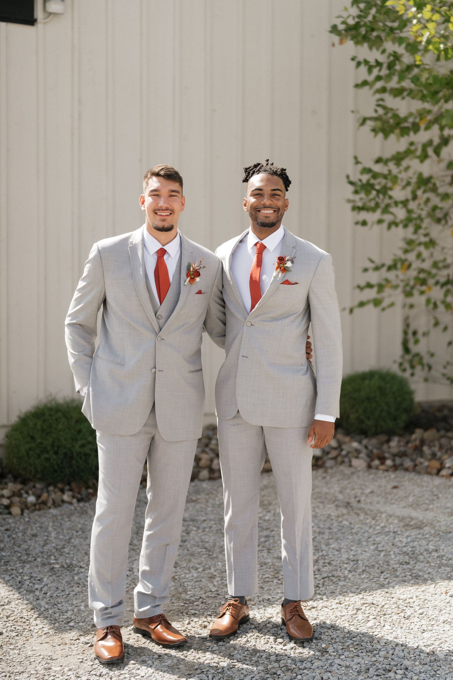 Groomsmen in matching light gray suits and red ties pose on a gravel path.