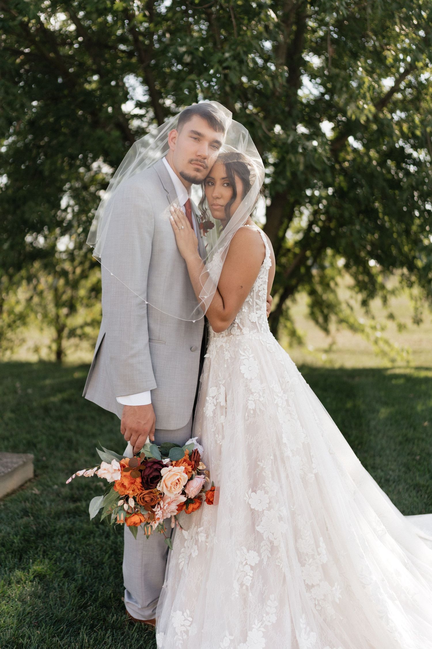 Intimate wedding couple portraits under trees with lace dress and gray suit details.