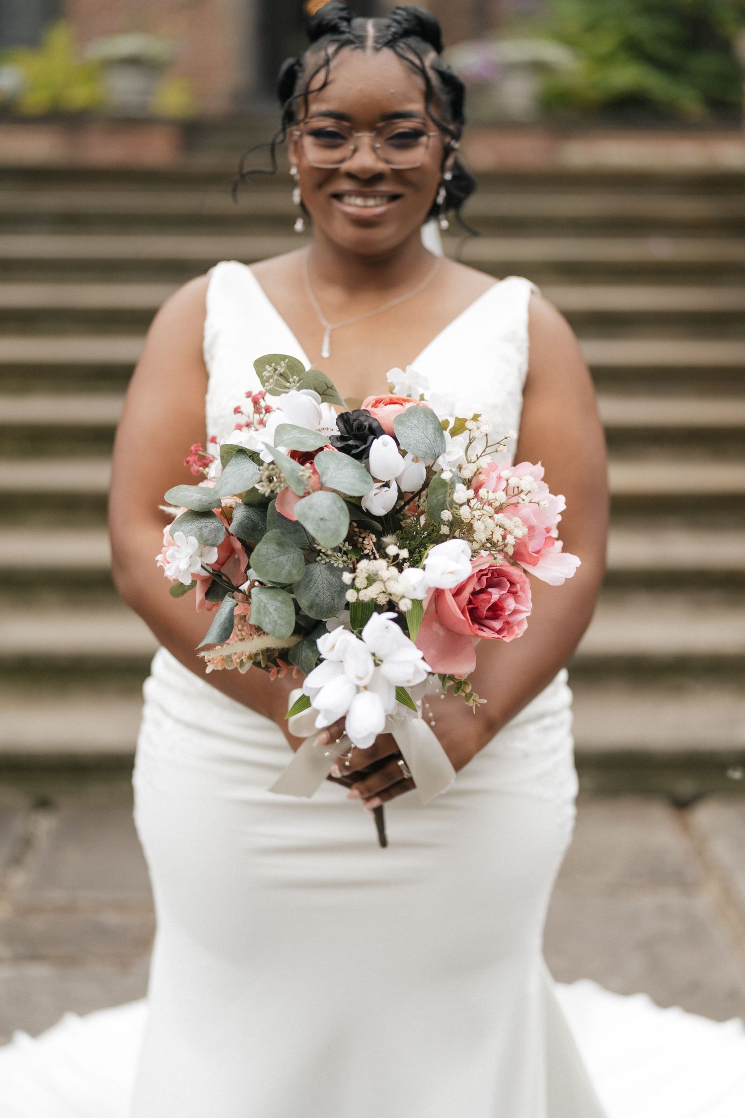A beautiful wedding bouquet features pink roses, white flowers and eucalyptus leaves against a formal dress.
