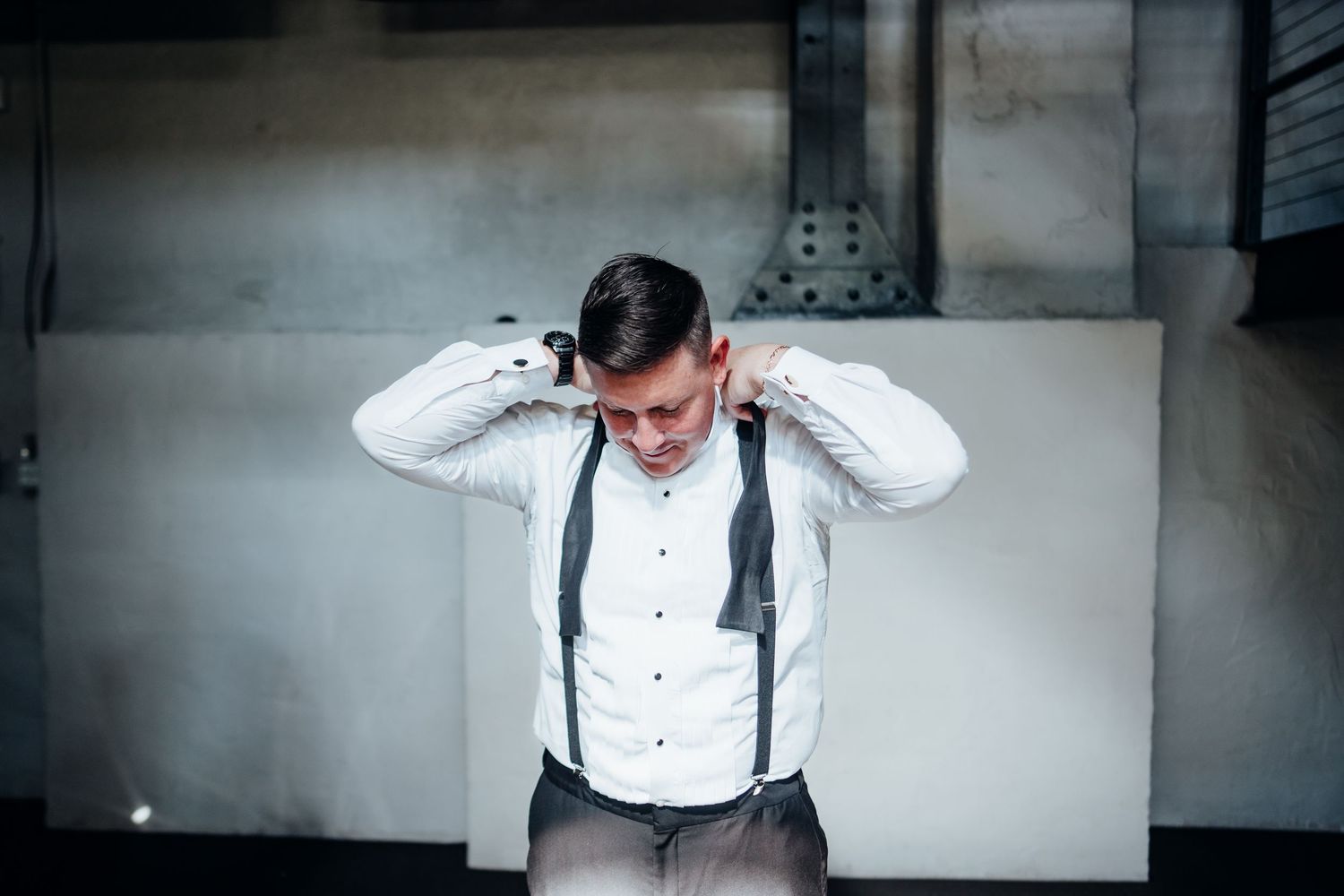Wedding party member adjusting formal attire against white wall.