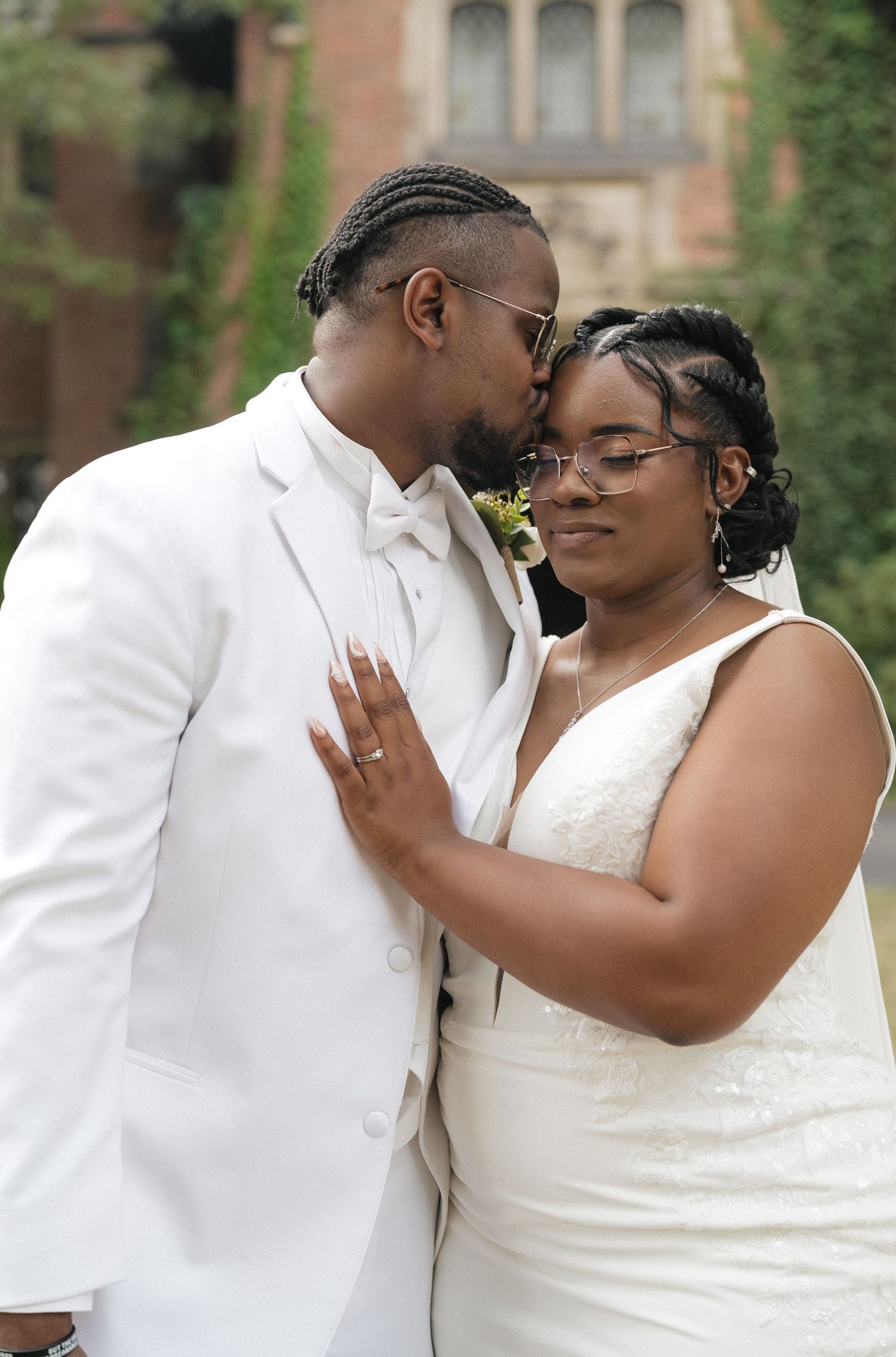 Romantic wedding couple embraces outdoors against brick building backdrop.
