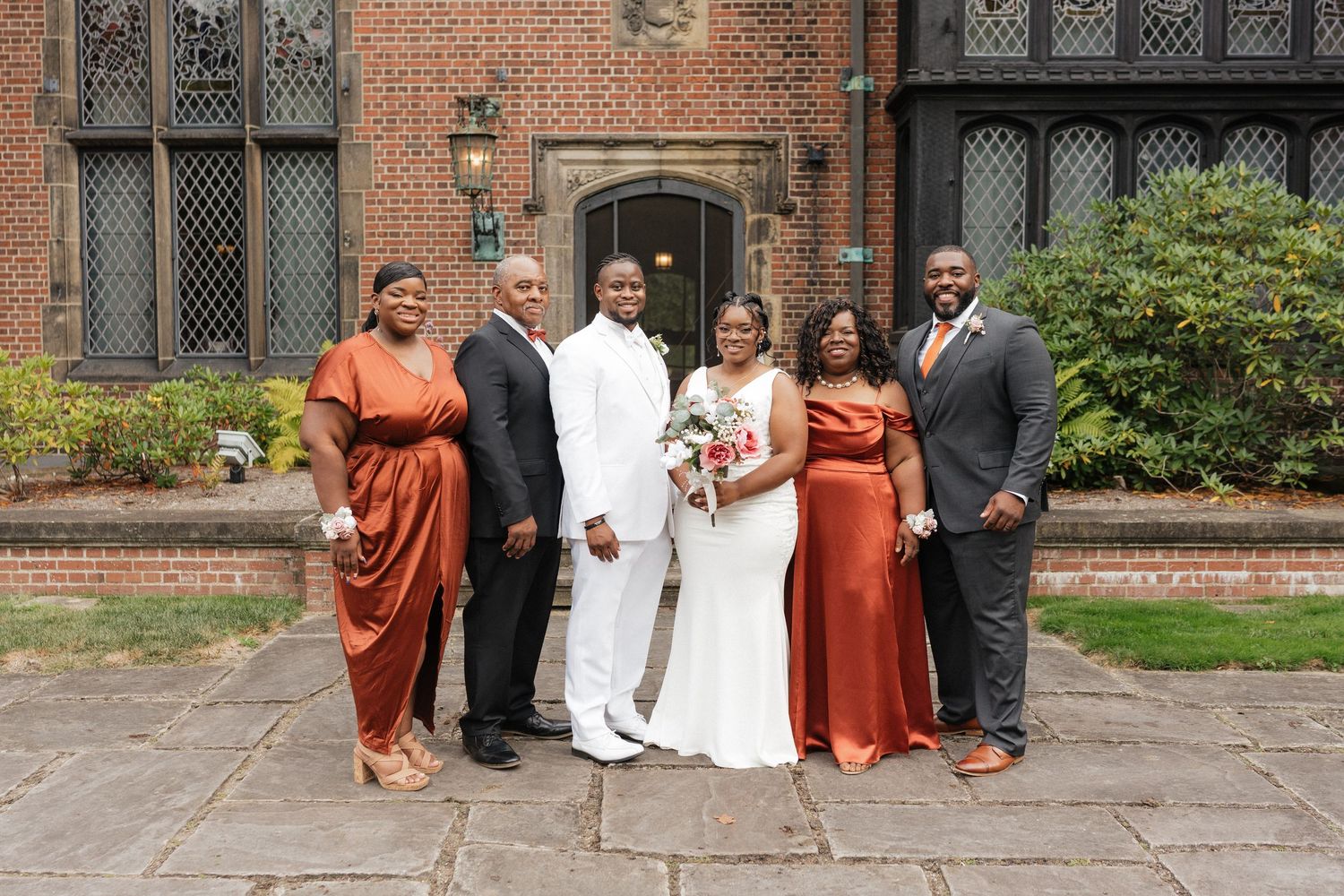 Wedding party poses on brick steps wearing white and burnt orange attire.