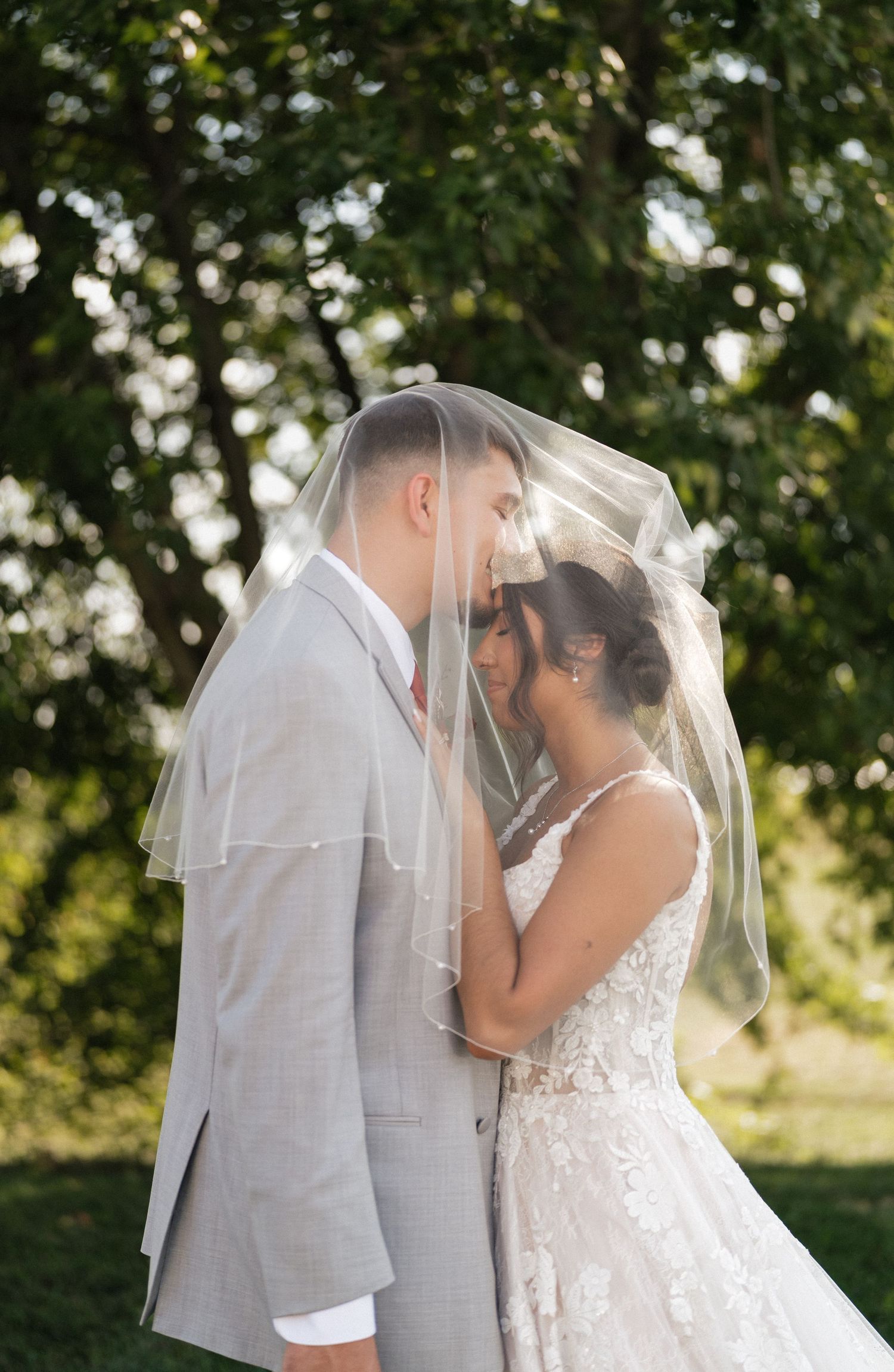 Intimate wedding portraits showing tender moments between newlyweds under a veil in natural lighting.