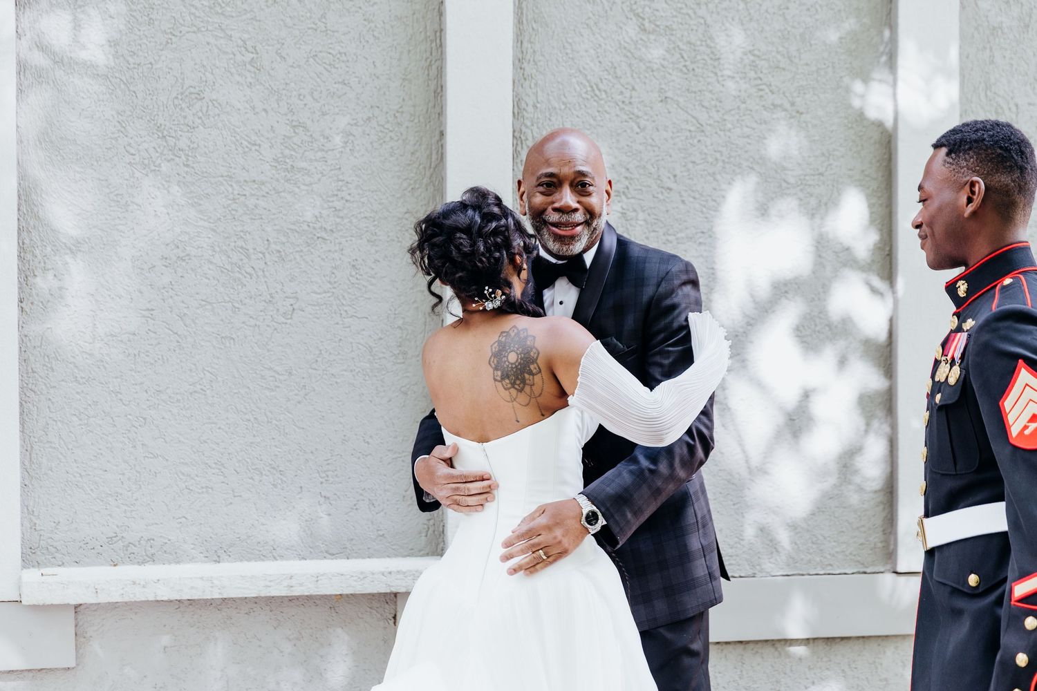 Wedding party members share joyful moments outside a white building with natural lighting.