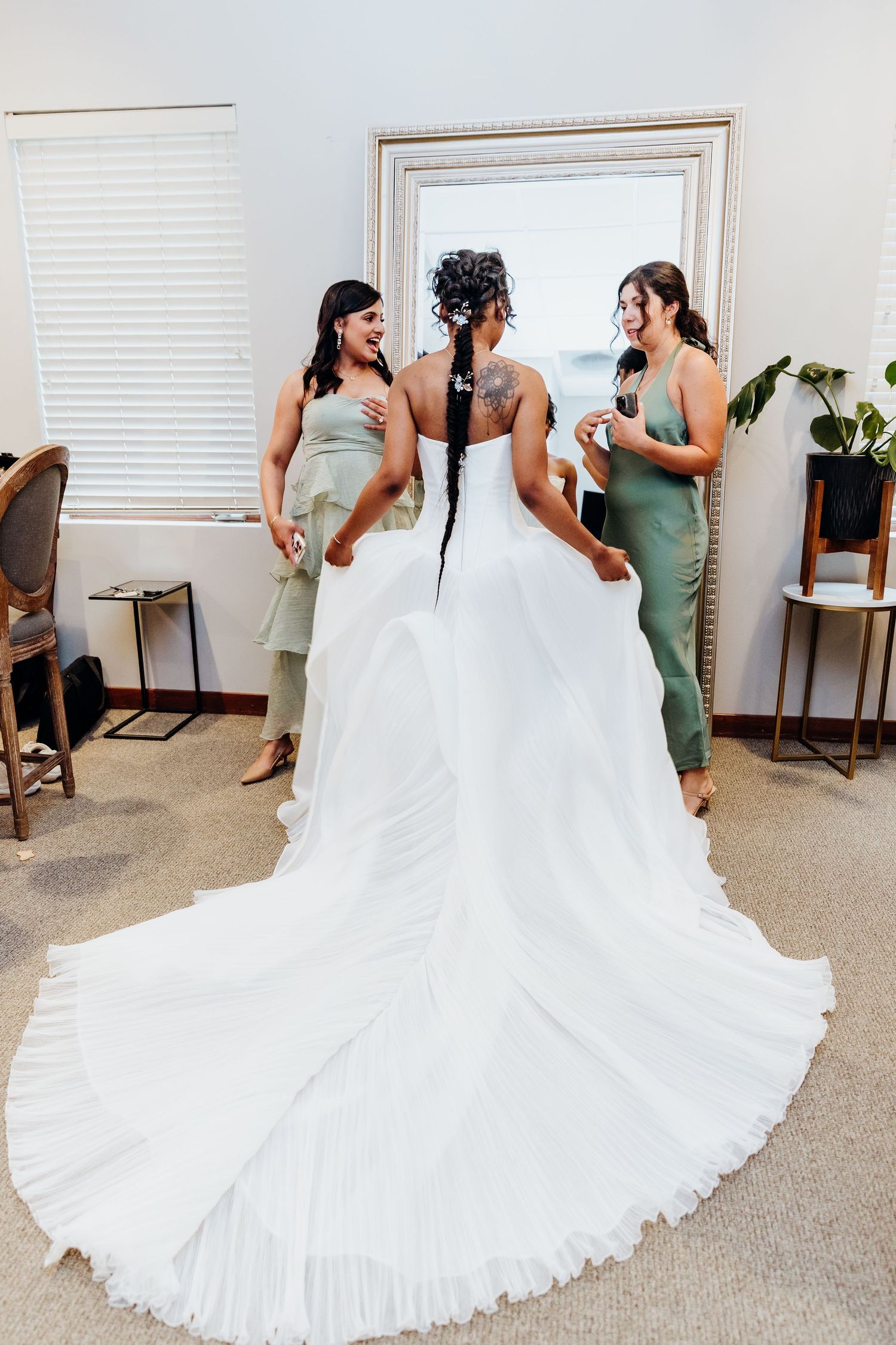 Bridesmaids in sage green dresses assist with a stunning white wedding gown featuring a dramatic cathedral-length train.