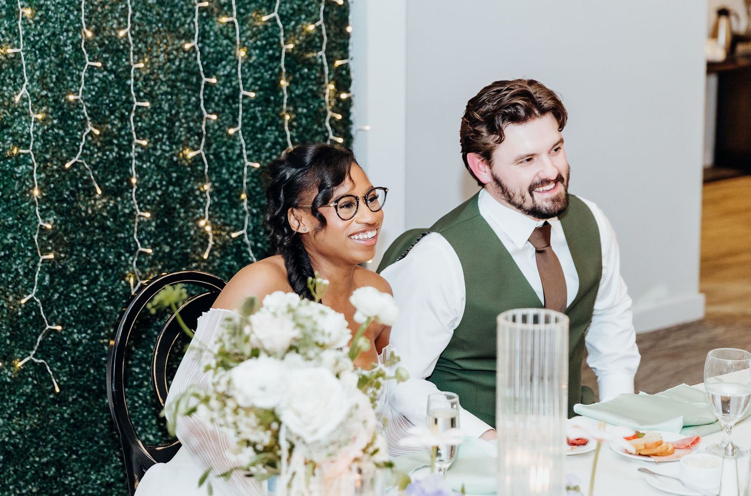 Wedding reception dinner with elegant table settings and decorative marble wall backdrop.