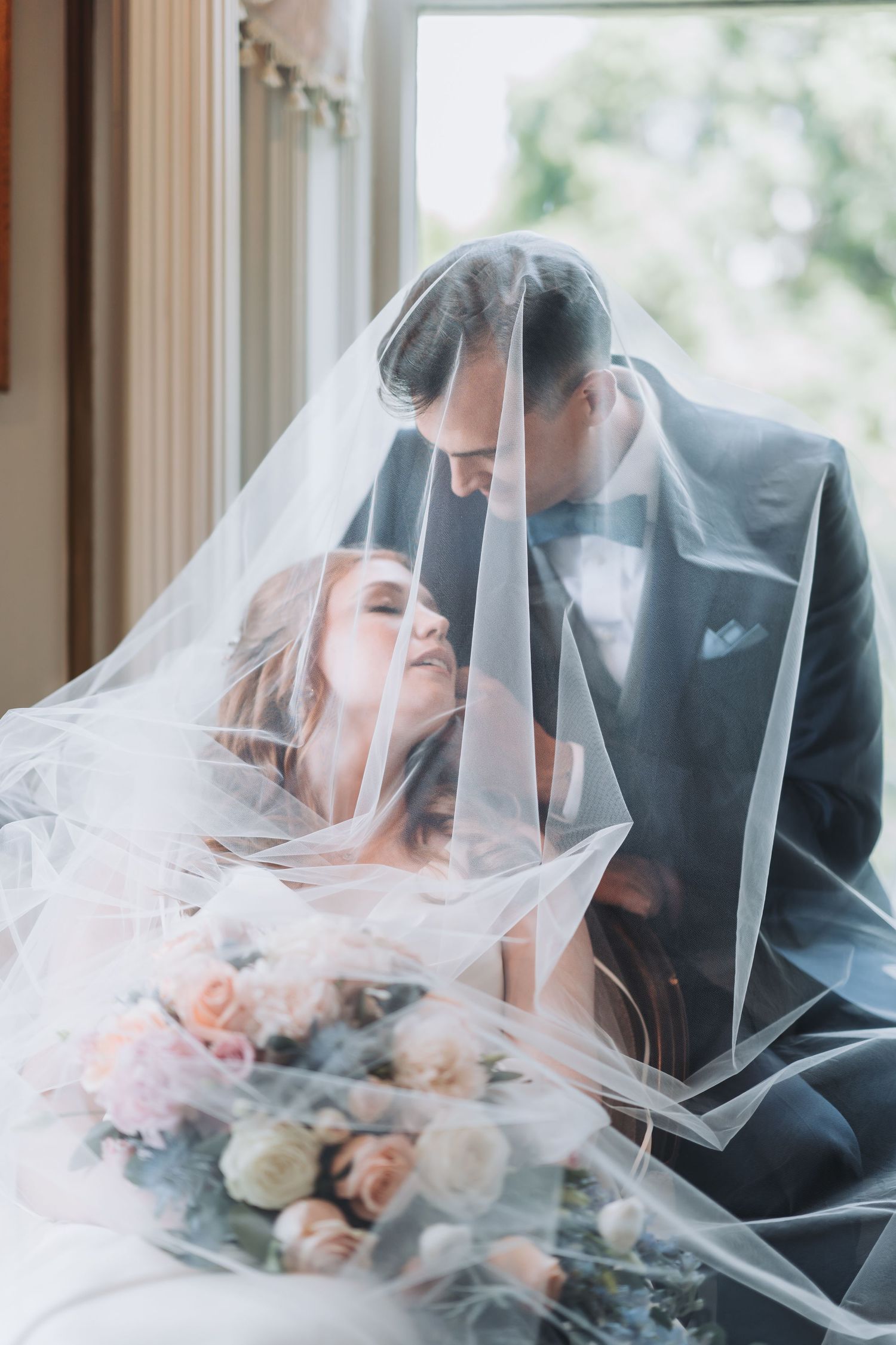 A tender wedding moment captured through a delicate veil with soft natural window light.