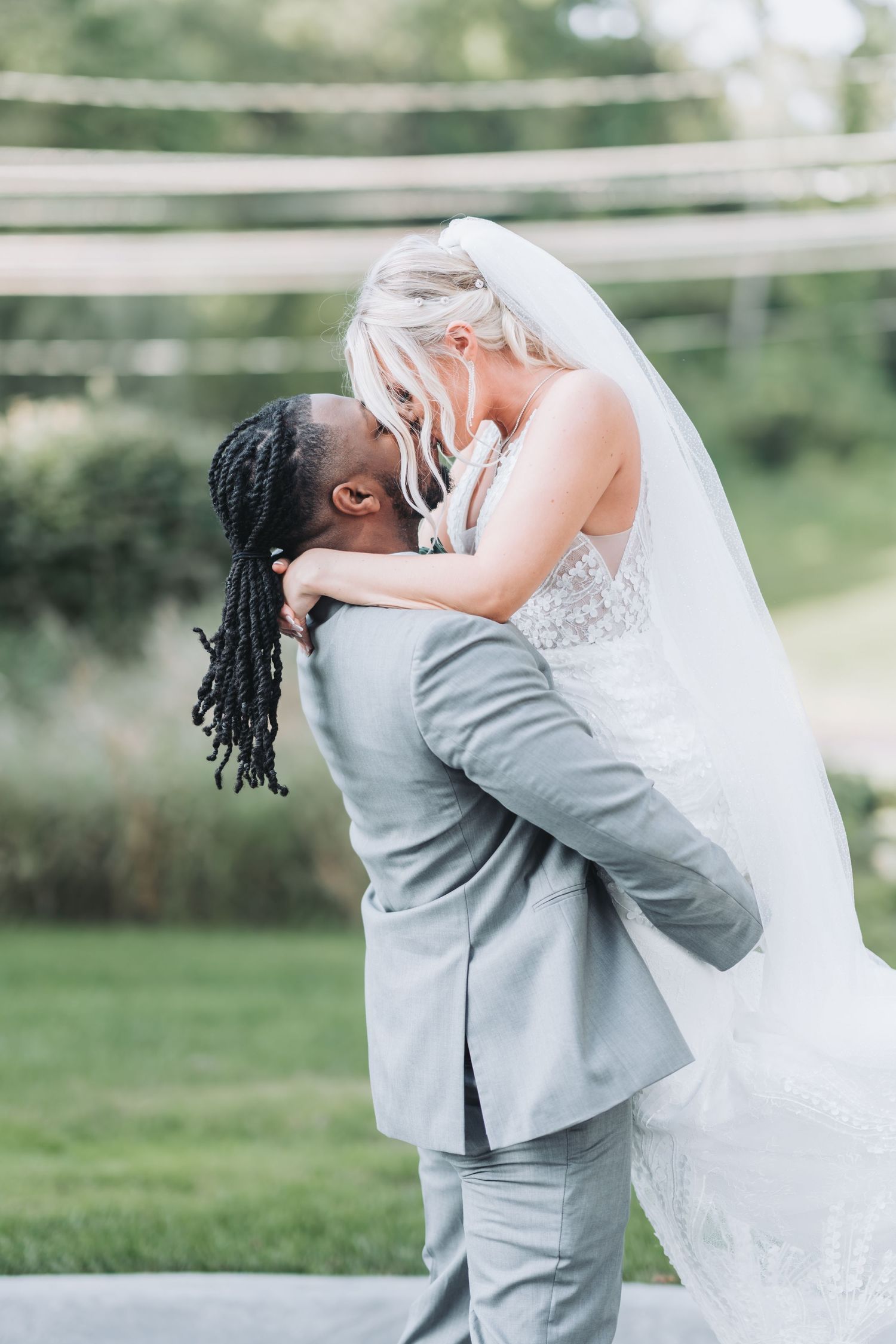 A couple shares a romantic embrace in their wedding attire against a soft, natural outdoor backdrop.