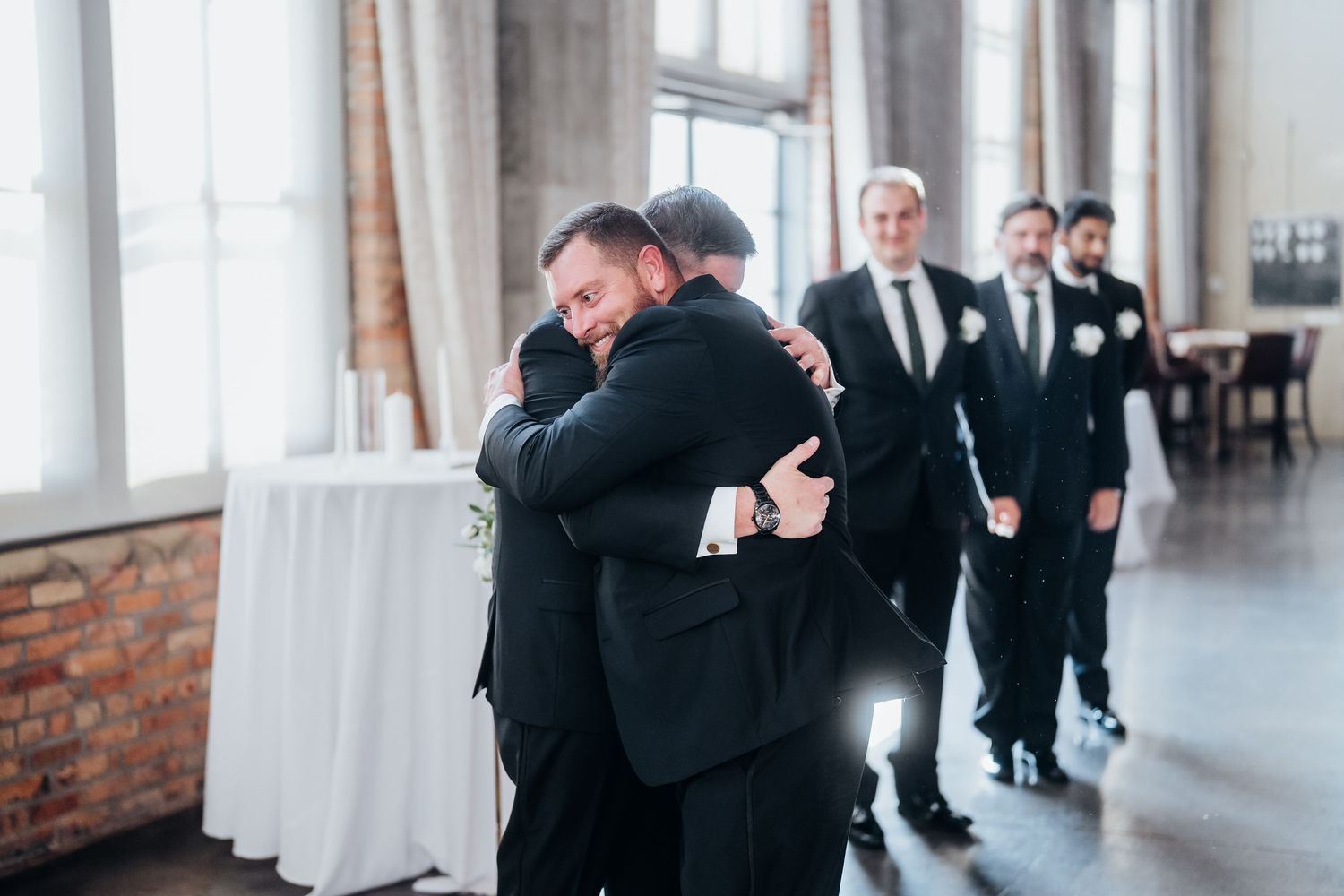 Wedding party members share emotional embraces in a bright modern venue.