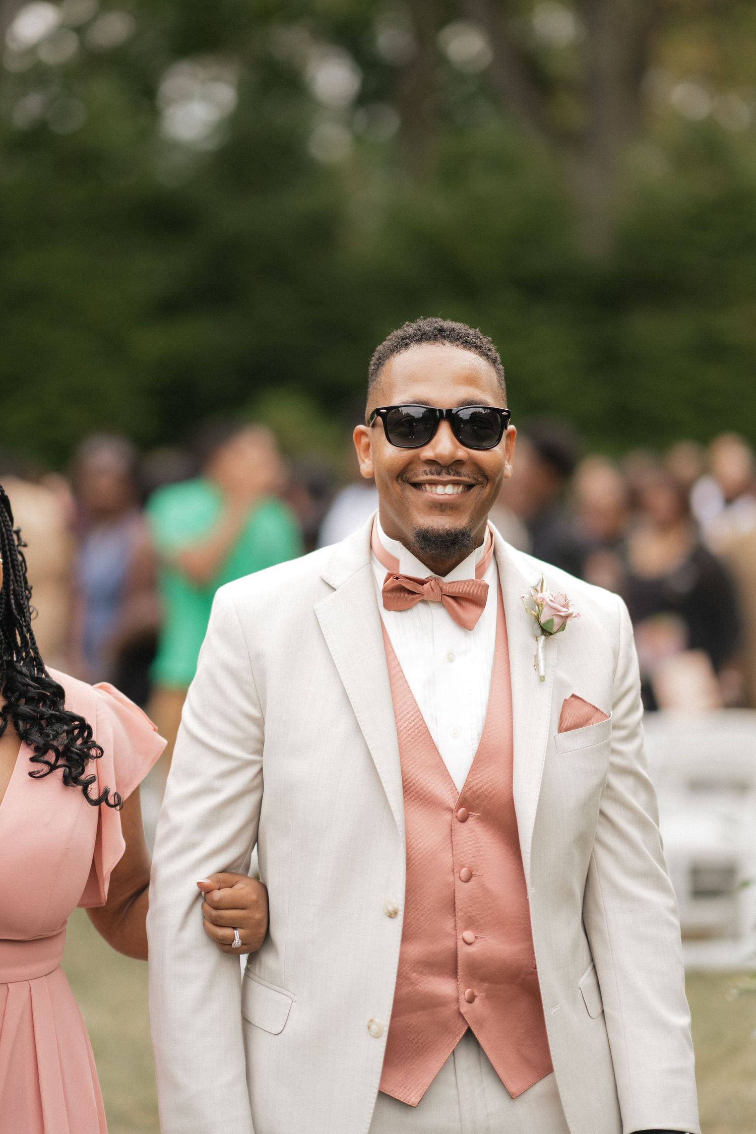 Groomsmen in white suits with peach vests pose together at an outdoor wedding.