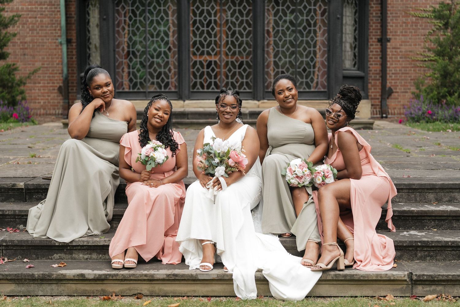 Bridal party in pastel dresses poses on stone steps of historic building.