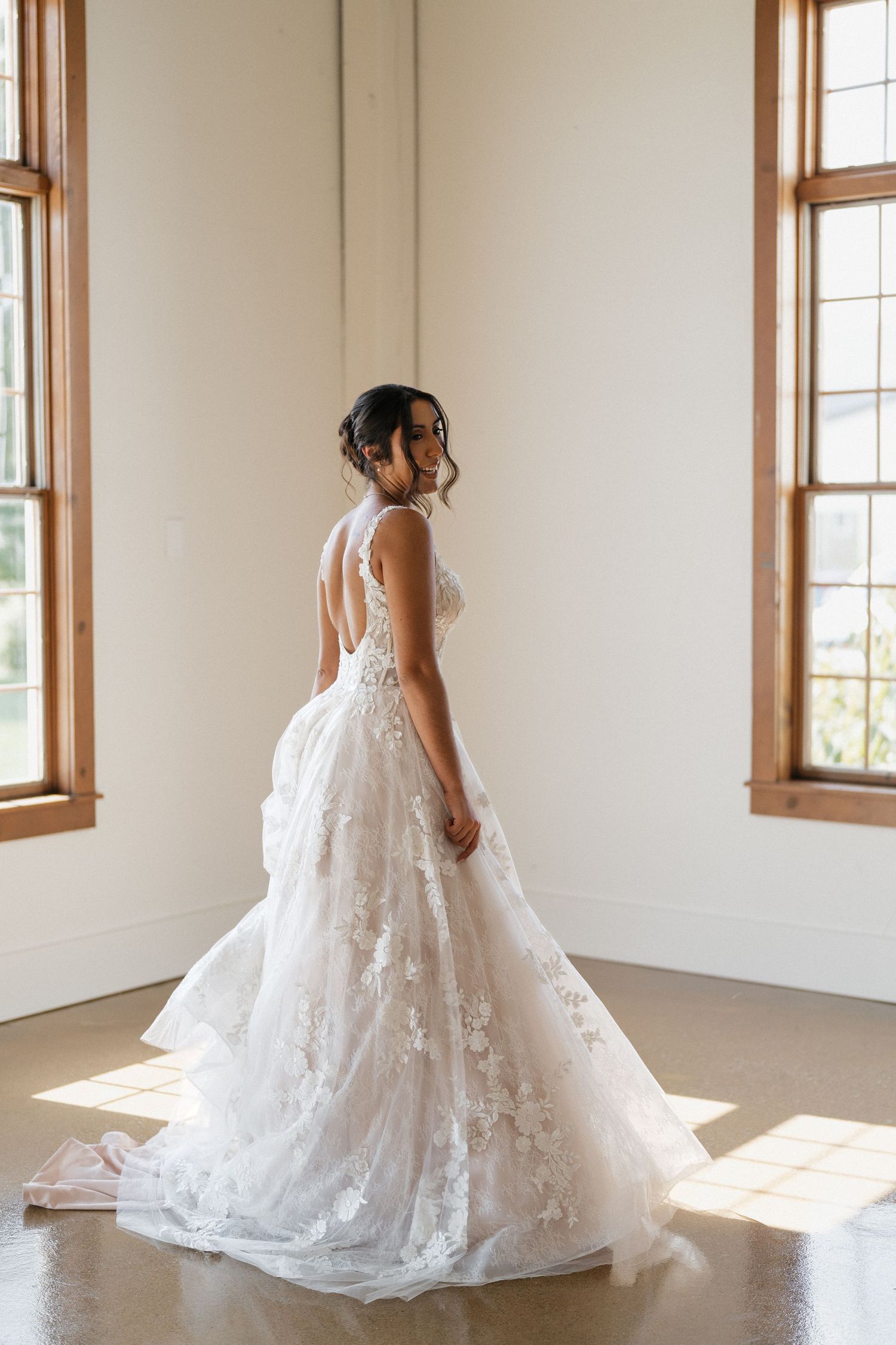 A flowing white lace wedding gown with train photographed in natural window light.