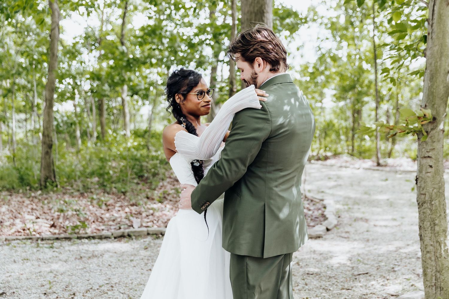 Couple embraces during intimate wedding moment on outdoor stone pathway surrounded by trees.