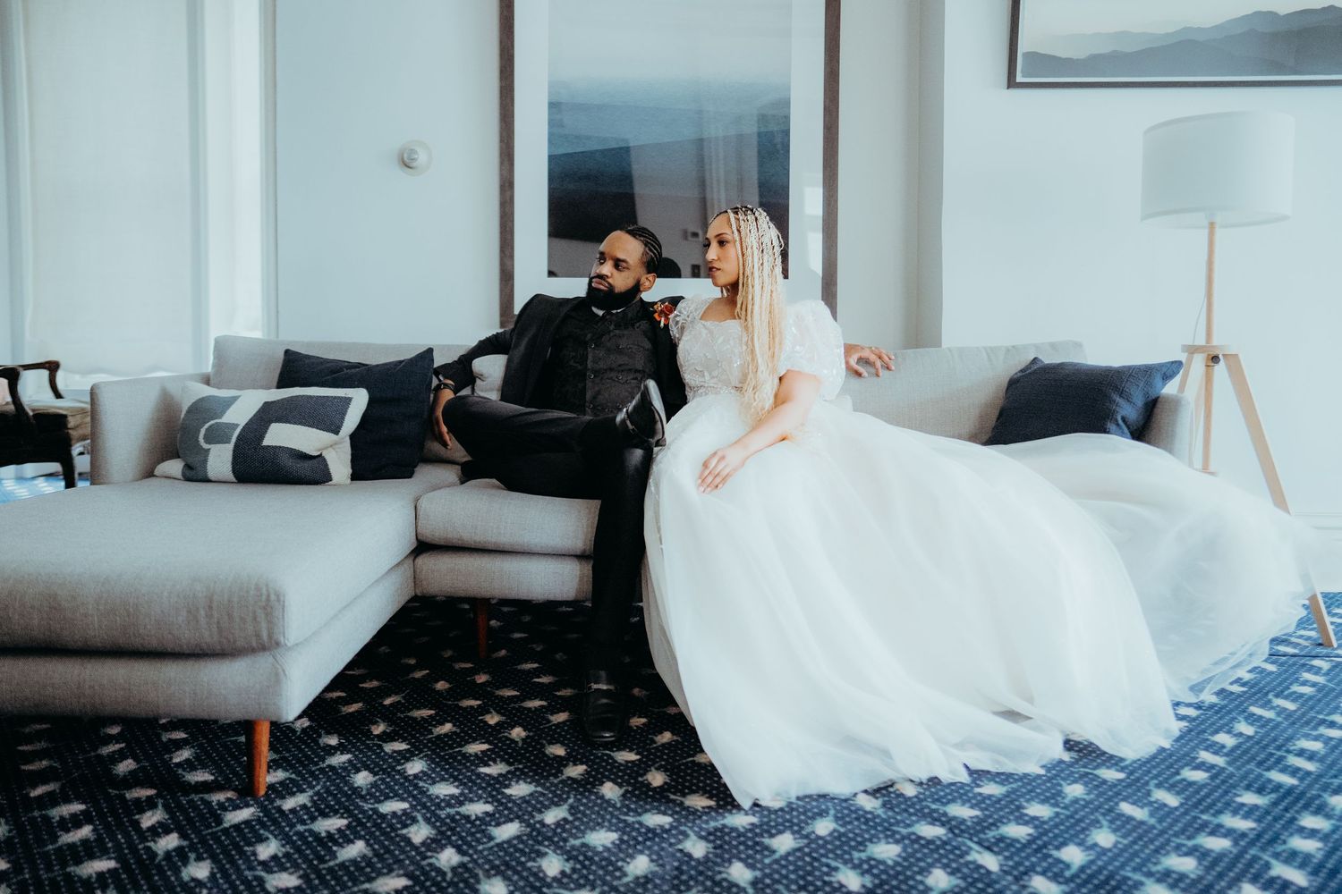 A couple relaxes on a modern gray sectional sofa with a patterned blue carpet.