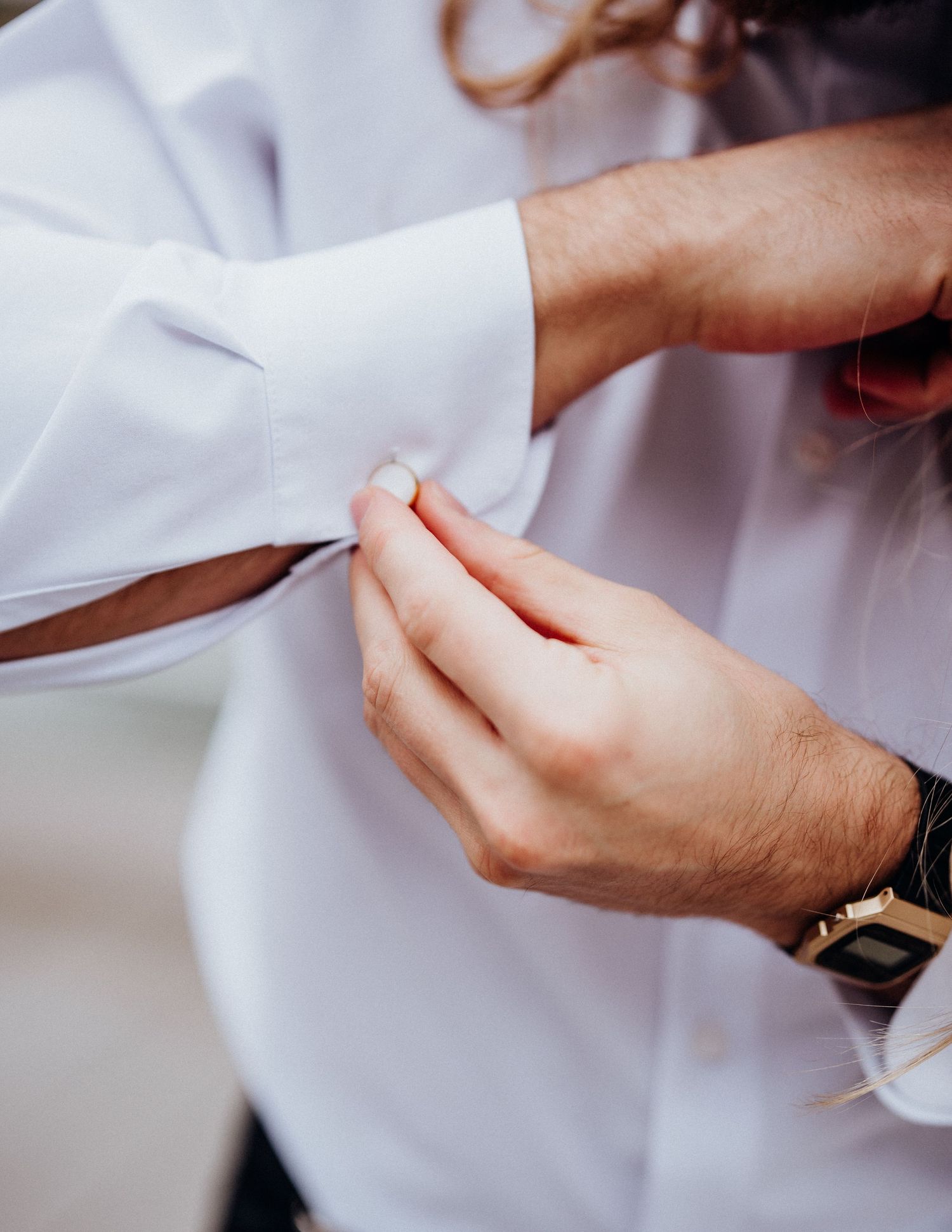 Close-up shot of hands fastening a white dress shirt cuff button.