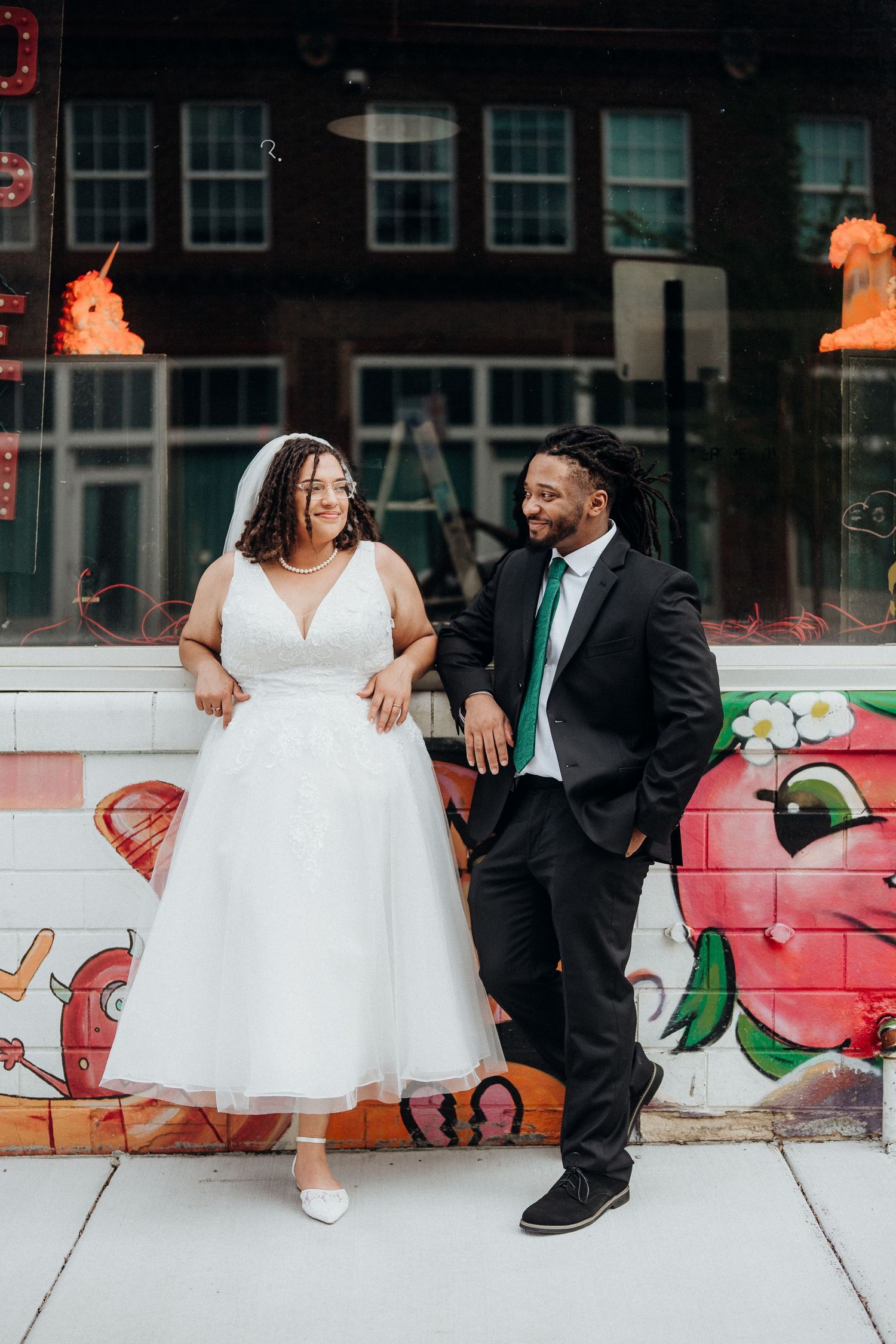 A couple in wedding attire poses against a colorful graffiti wall.