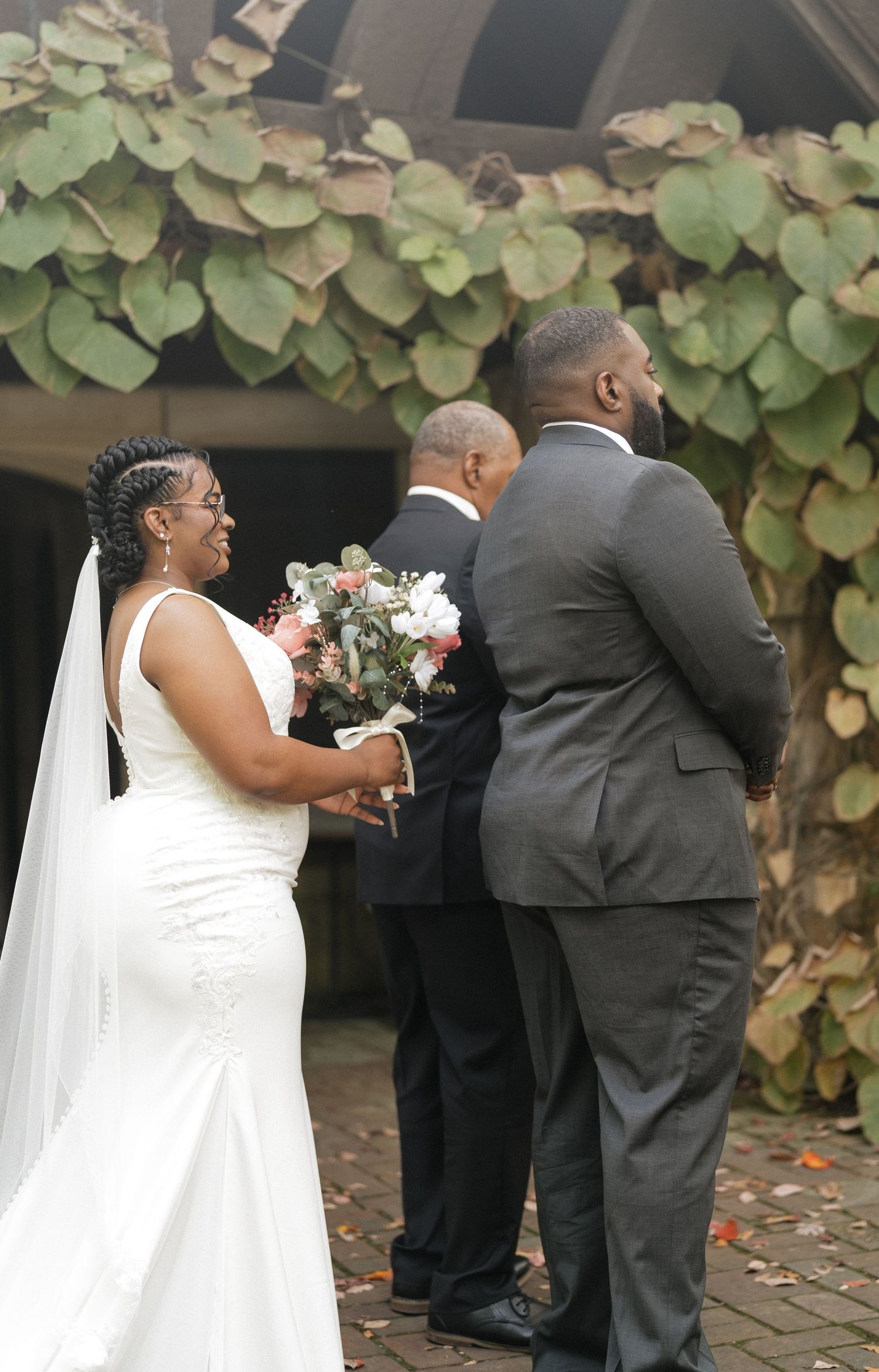 Wedding party members in formal attire gather during an outdoor ceremony with lush foliage in the background.